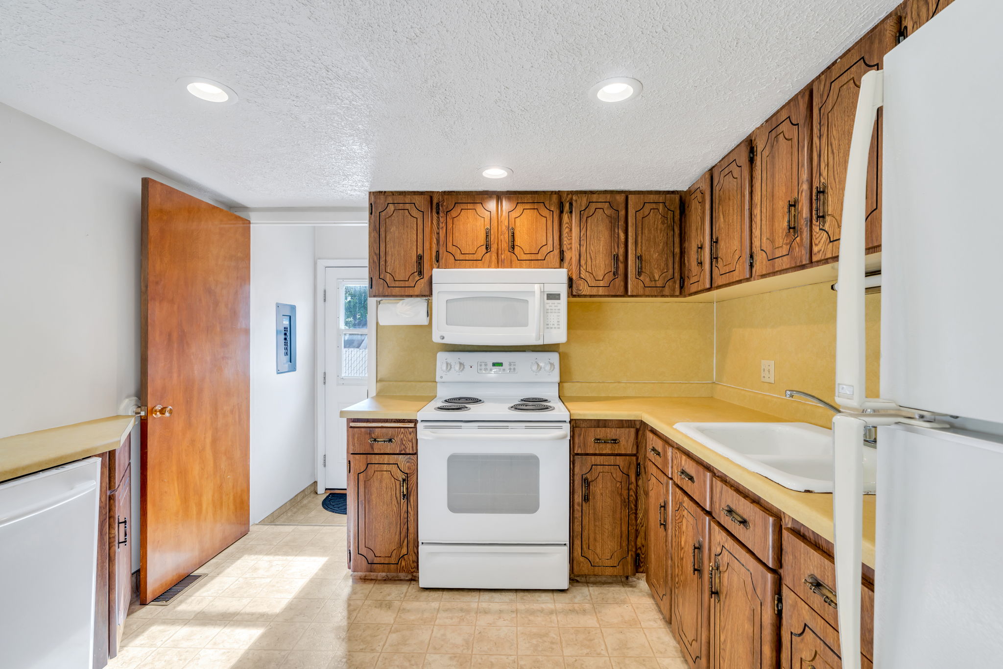Kitchen featuring wood cabinetry, white appliances including a range and microwave, a double basin sink, and recessed ceiling lighting