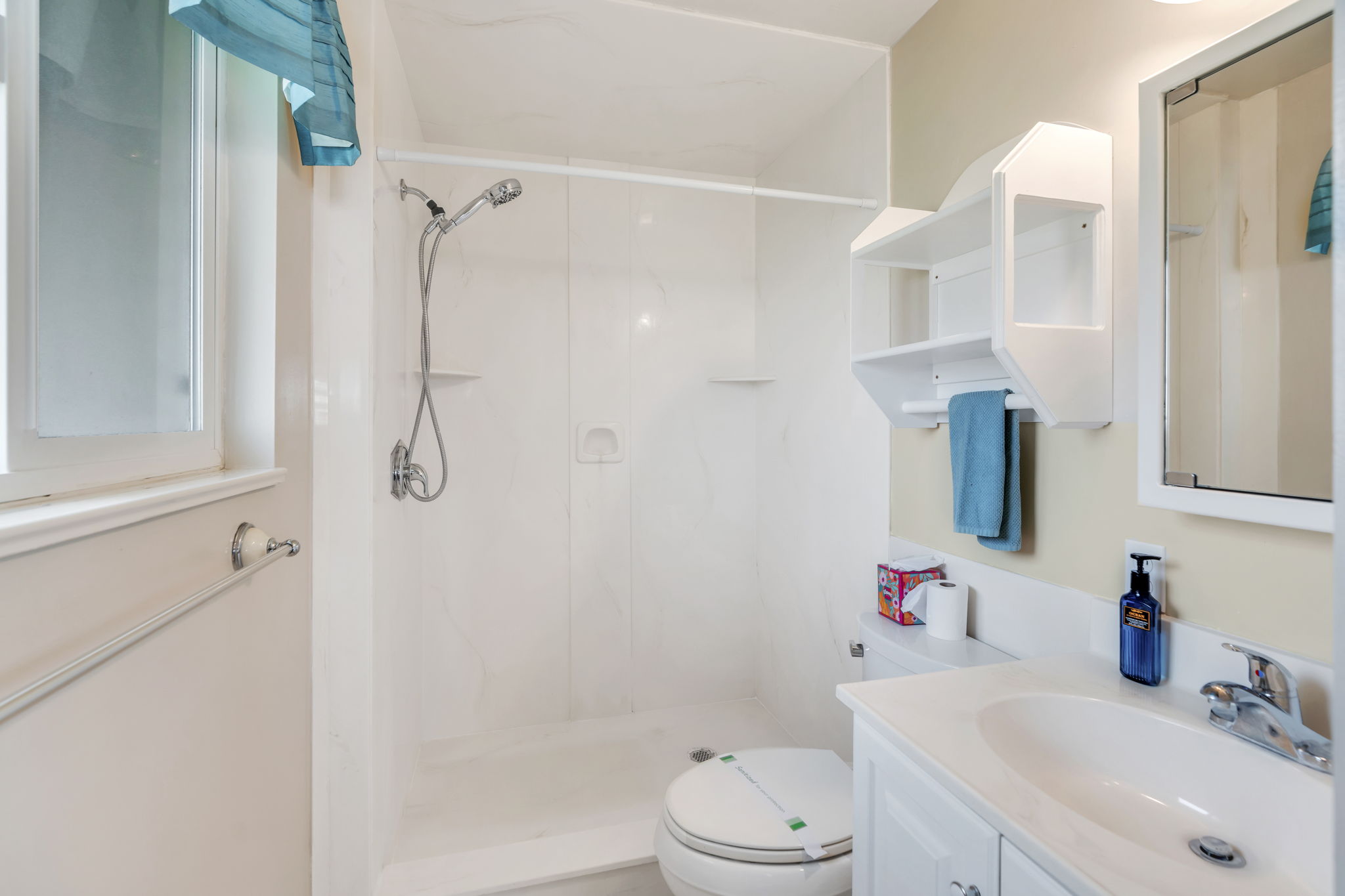 Primary Bathroom featuring a white shower stall with a handheld showerhead, a single window, a vanity with an integrated sink, a wall-mounted medicine cabinet, and a toilet