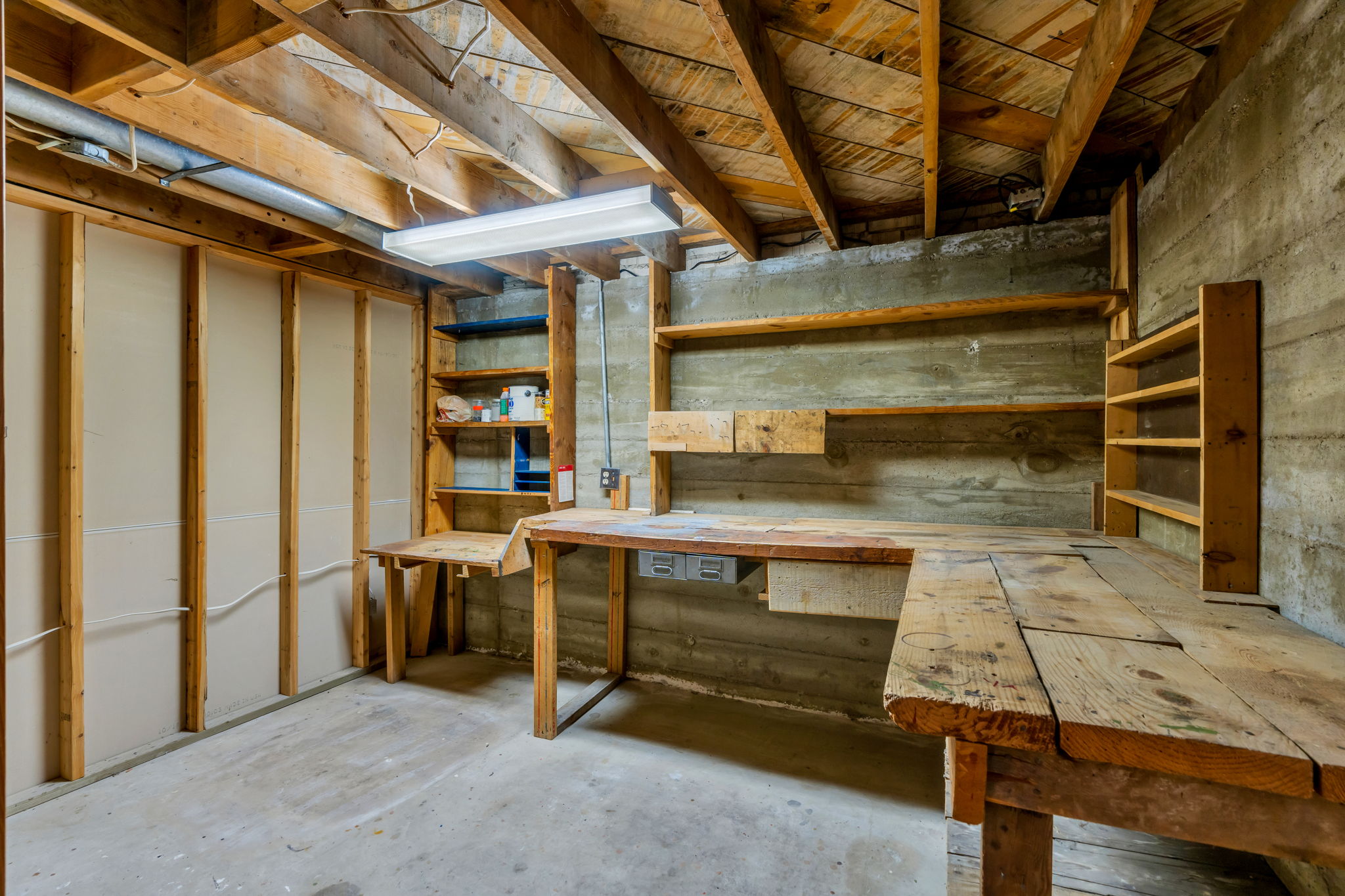 Basement workshop area featuring concrete walls and an exposed wood beam ceiling