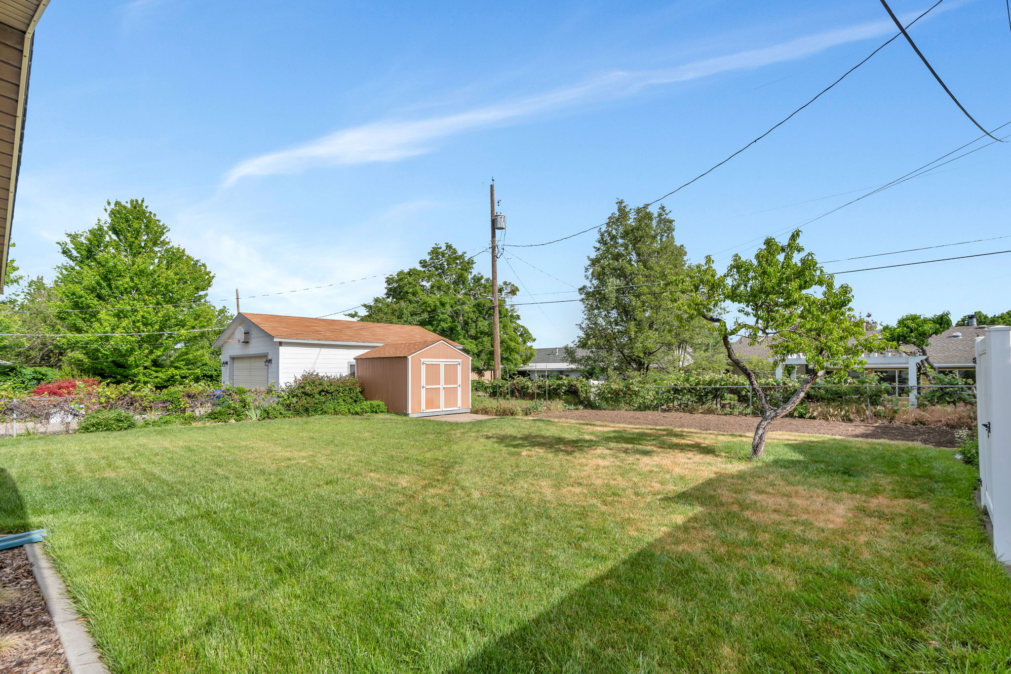 Expansive backyard featuring a large green lawn, detached garage, and a separate storage shed
