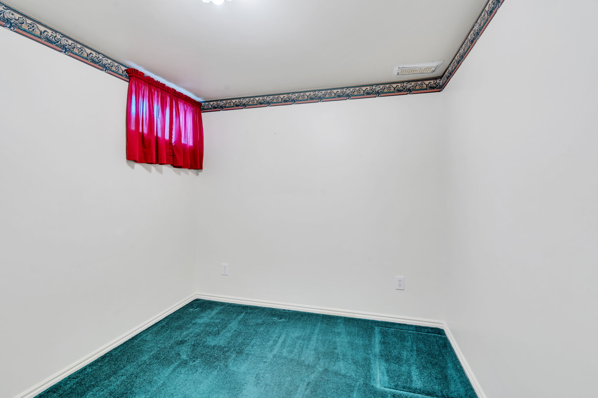 White walls with a decorative border trim, teal carpeting, and a single window with a red curtain