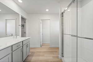 **Disclaimer**  Interior package may vary. Bathroom featuring a light wood-finish floor, dual vanity with light gray cabinetry and white countertops, and a clear glass enclosed shower with white subway tile