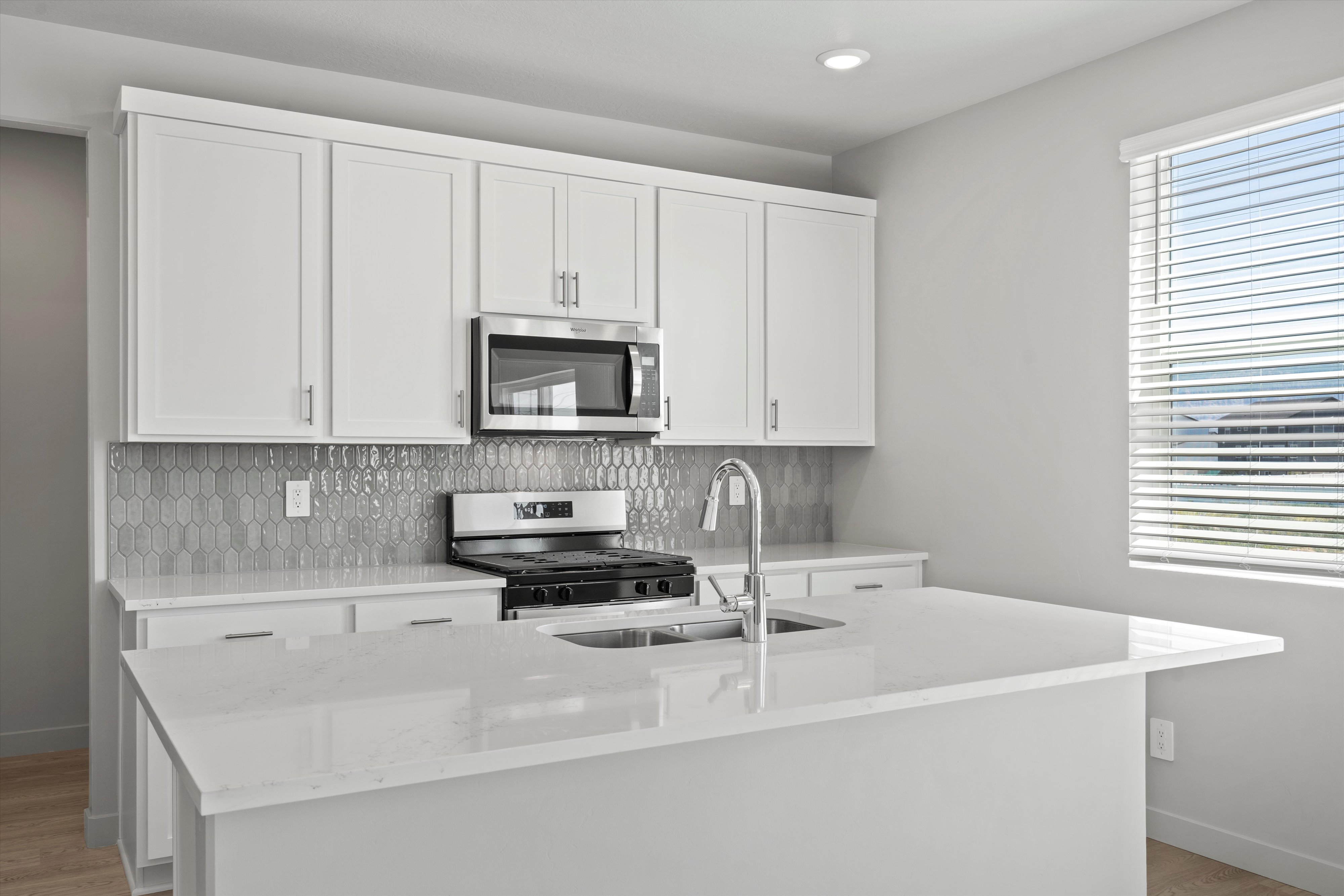 Kitchen featuring an island with an undermount sink, white cabinetry, a stainless steel microwave, a gas range, and a picket tile backsplash