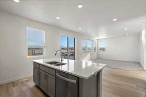 **Disclaimer**  Interior package may vary. Kitchen island featuring an undermount double sink with a gooseneck faucet, integrated dishwasher, and light-toned countertop