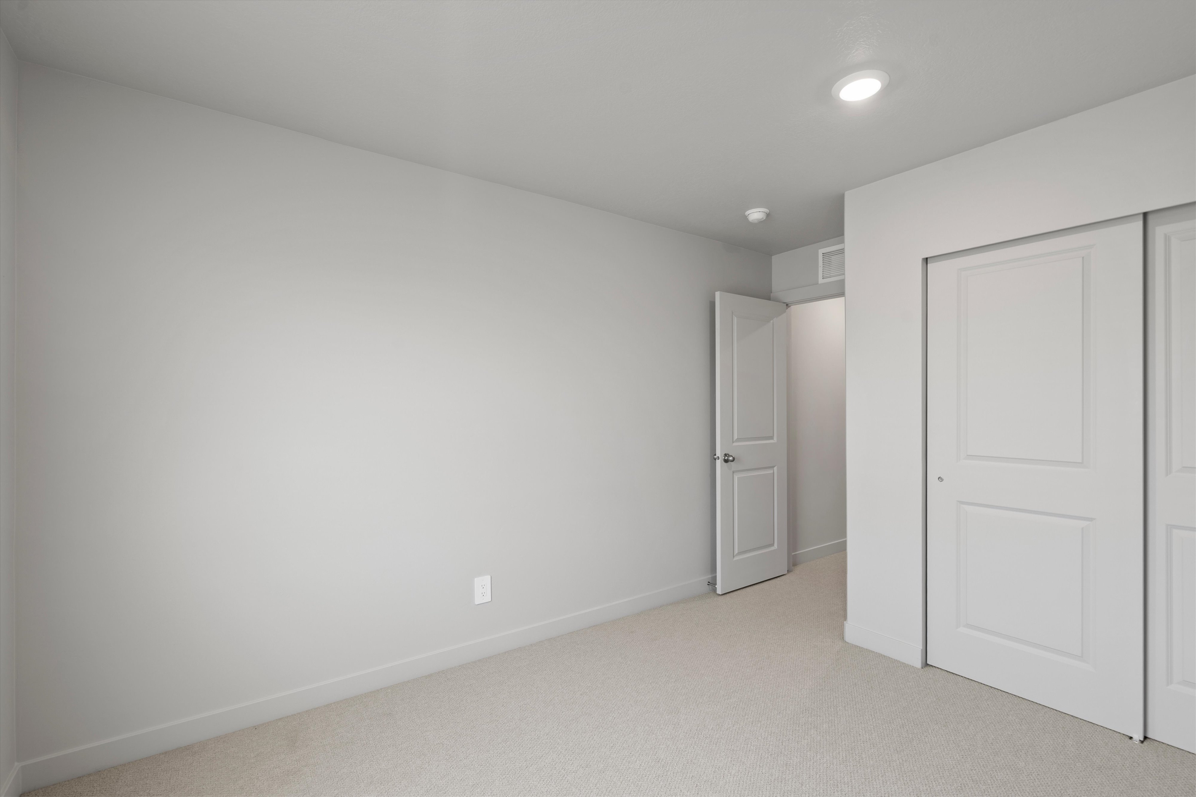 Neutral-toned room featuring light carpet, white baseboards, a white interior door, and two white sliding closet doors