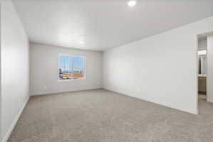 **Disclaimer**  Interior package may vary. Spacious room featuring neutral carpeting, recessed lighting, baseboard trim, a large window with blinds, and a doorway opening to a partial bathroom