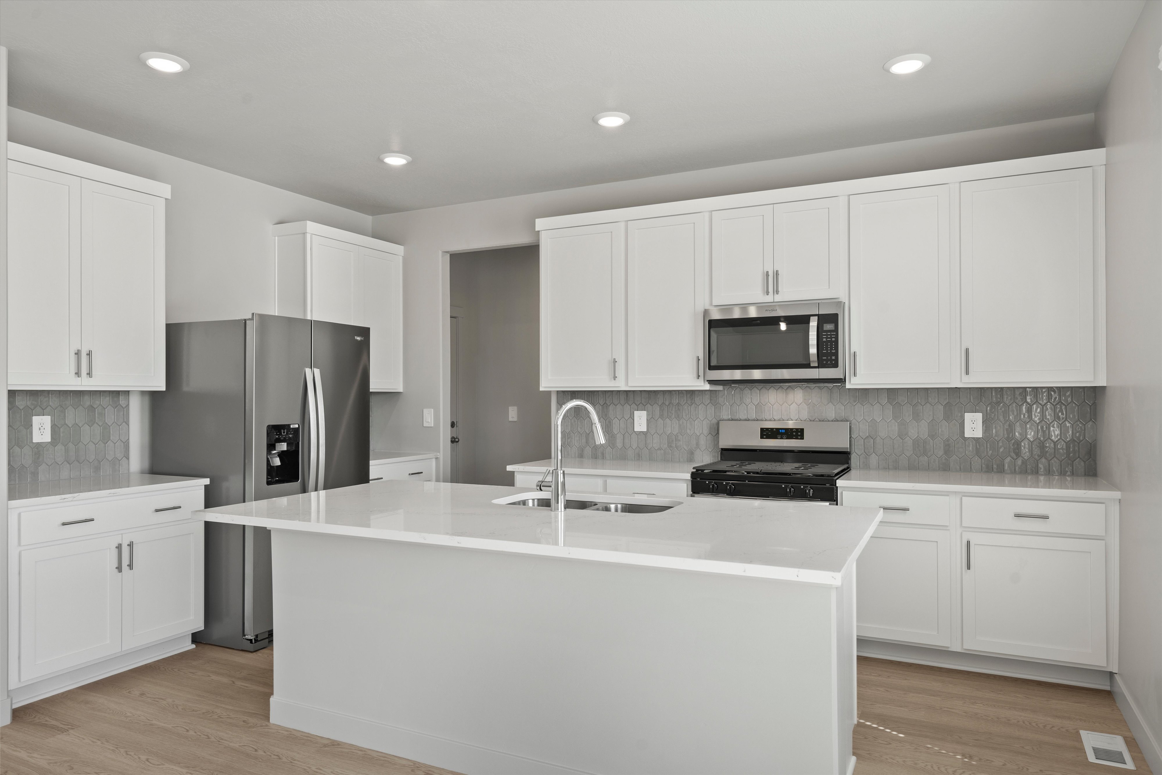 Modern kitchen featuring an expansive center island with an integrated sink, white cabinetry, stainless steel appliances, geometric tile backsplash, and recessed lighting