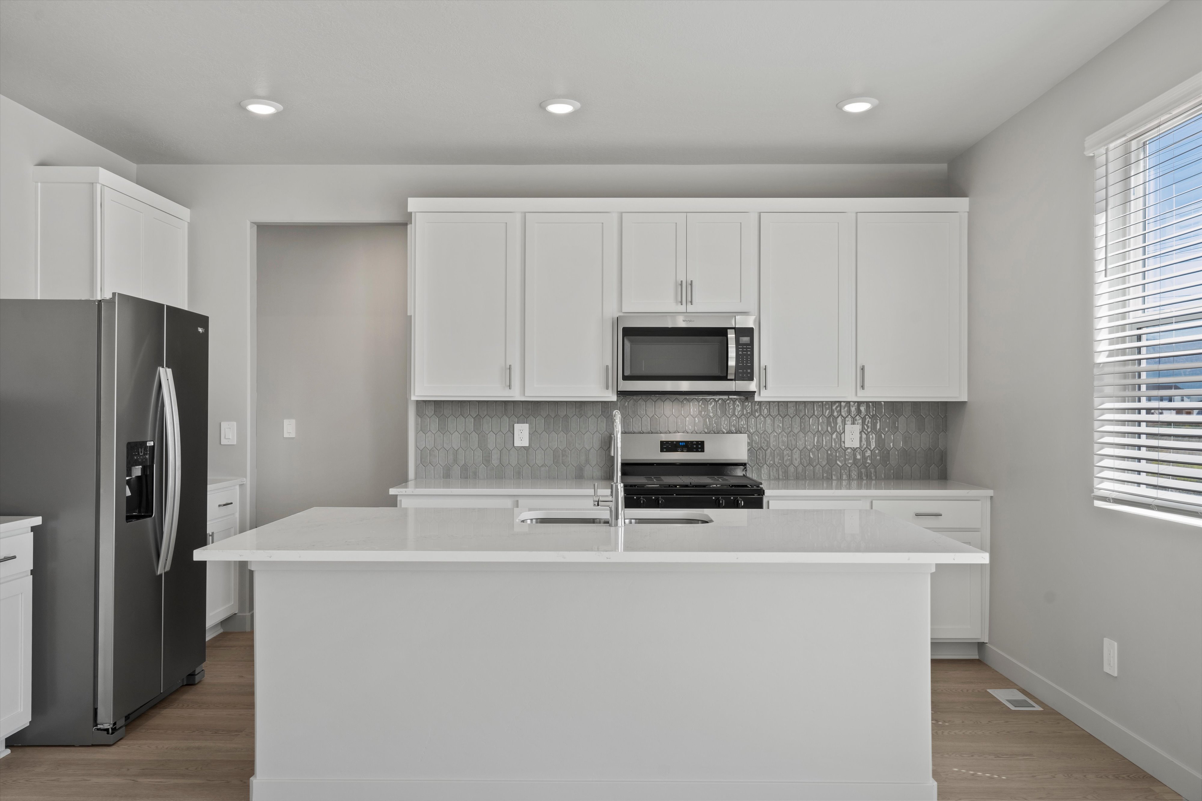 Contemporary kitchen featuring an expansive center island with an integrated sink, light-toned cabinetry, and stainless steel appliances