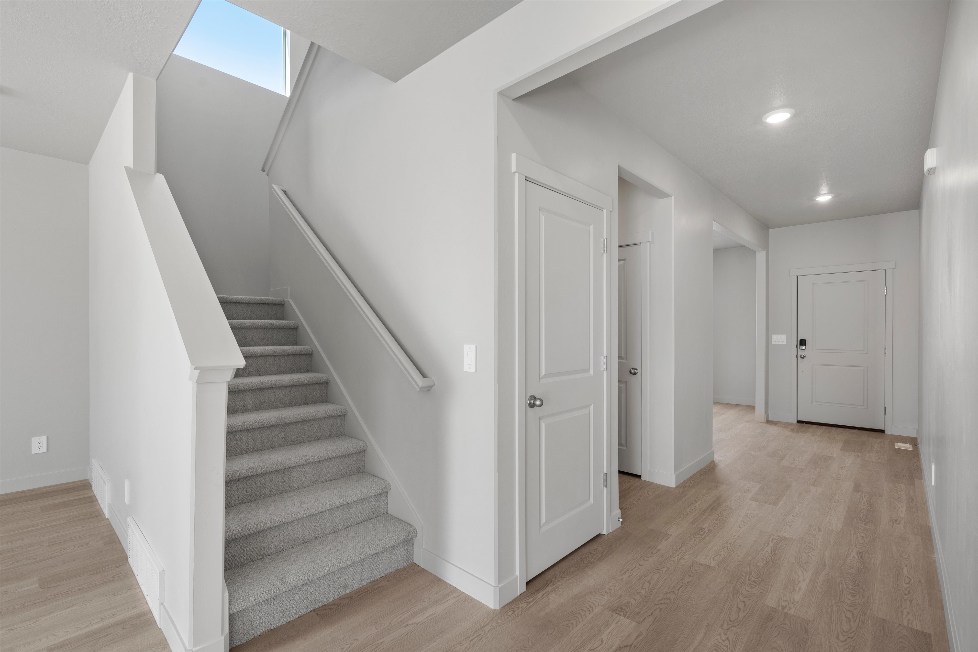 Inviting entryway featuring light wood-finish flooring, recessed lighting, and a staircase with carpeted treads and a skylight