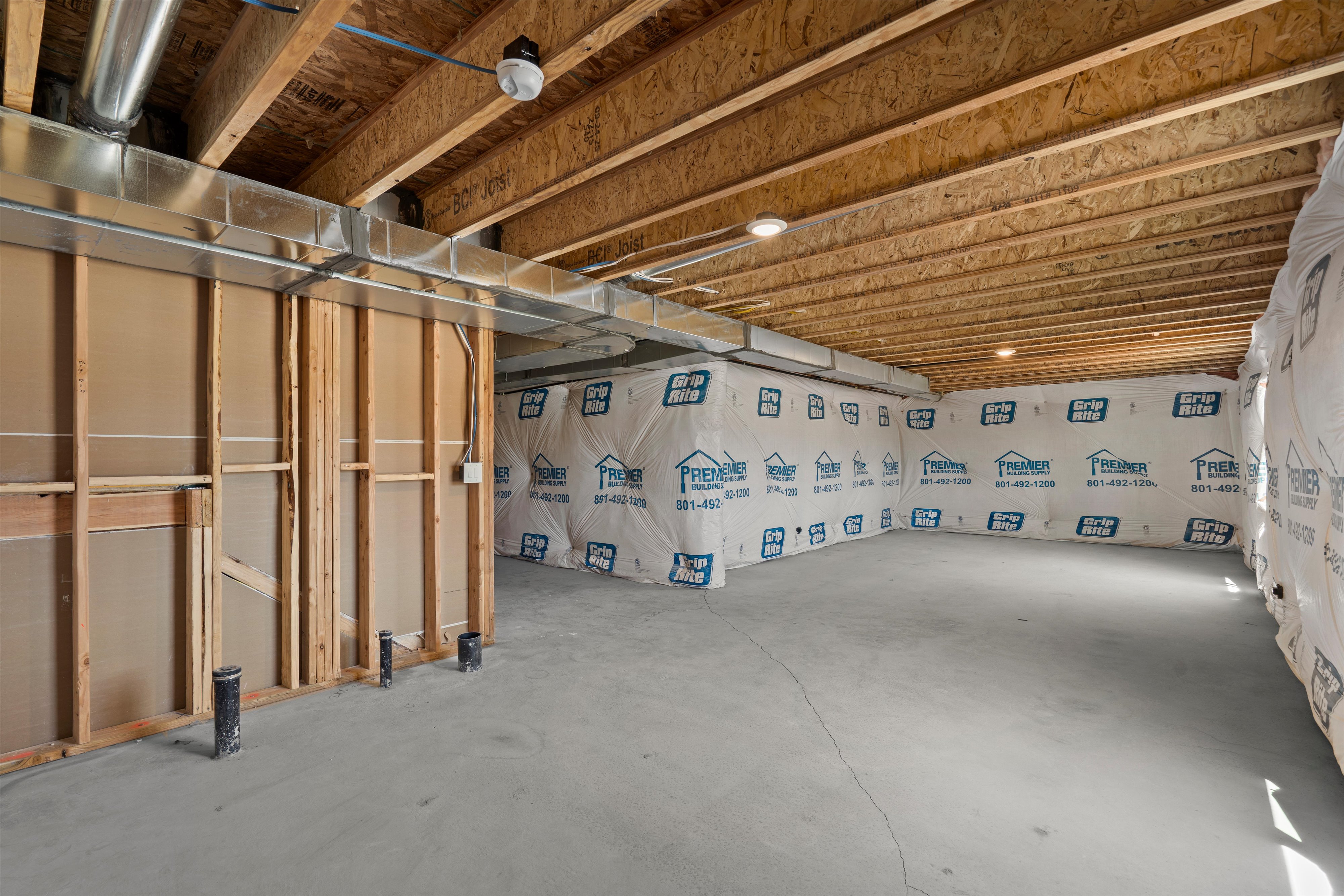 Unfinished basement featuring exposed wood joists, concrete flooring, insulated walls, and visible plumbing rough-ins