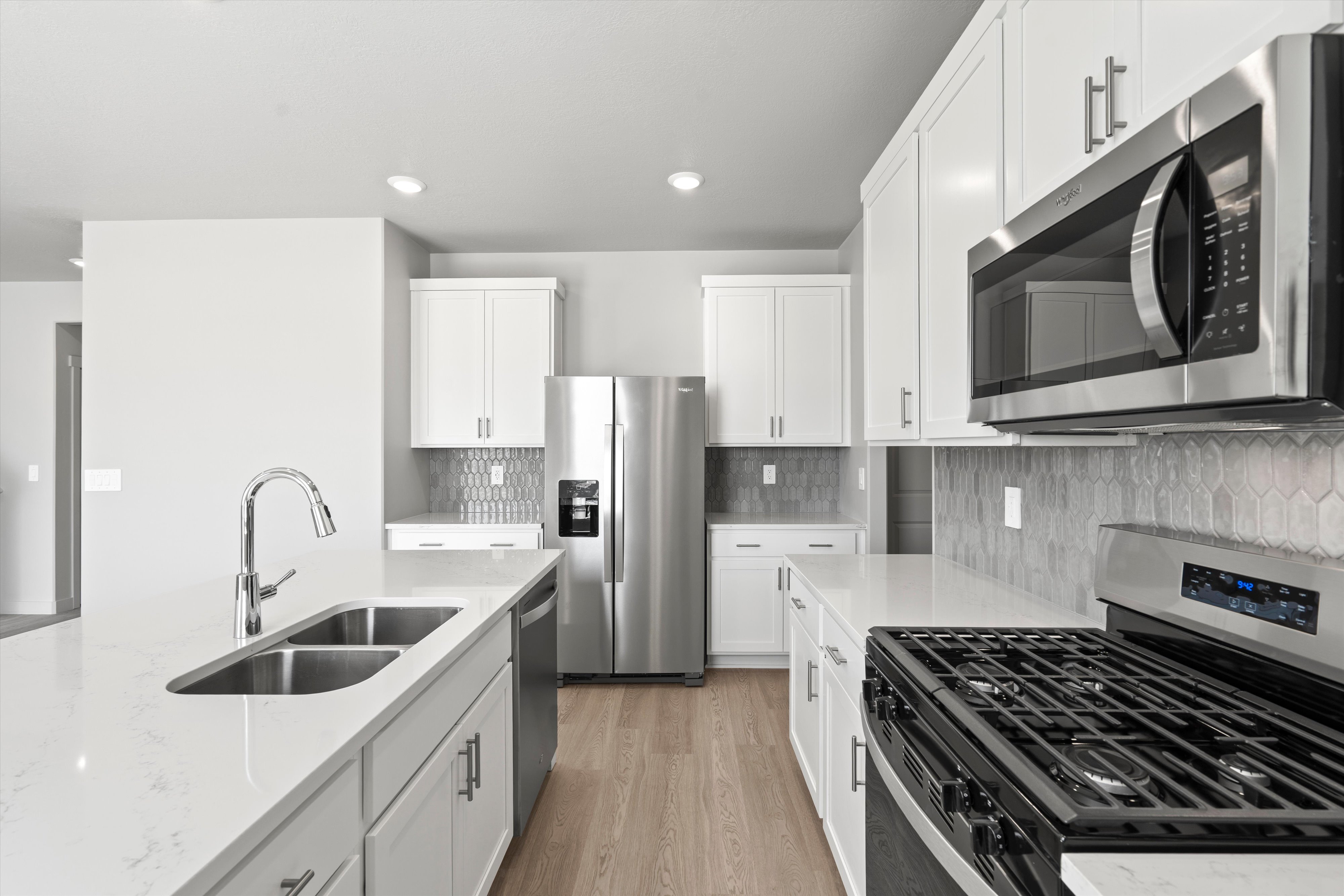 Modern kitchen featuring white cabinetry, stainless steel appliances, a double basin sink, and wood-finish flooring
