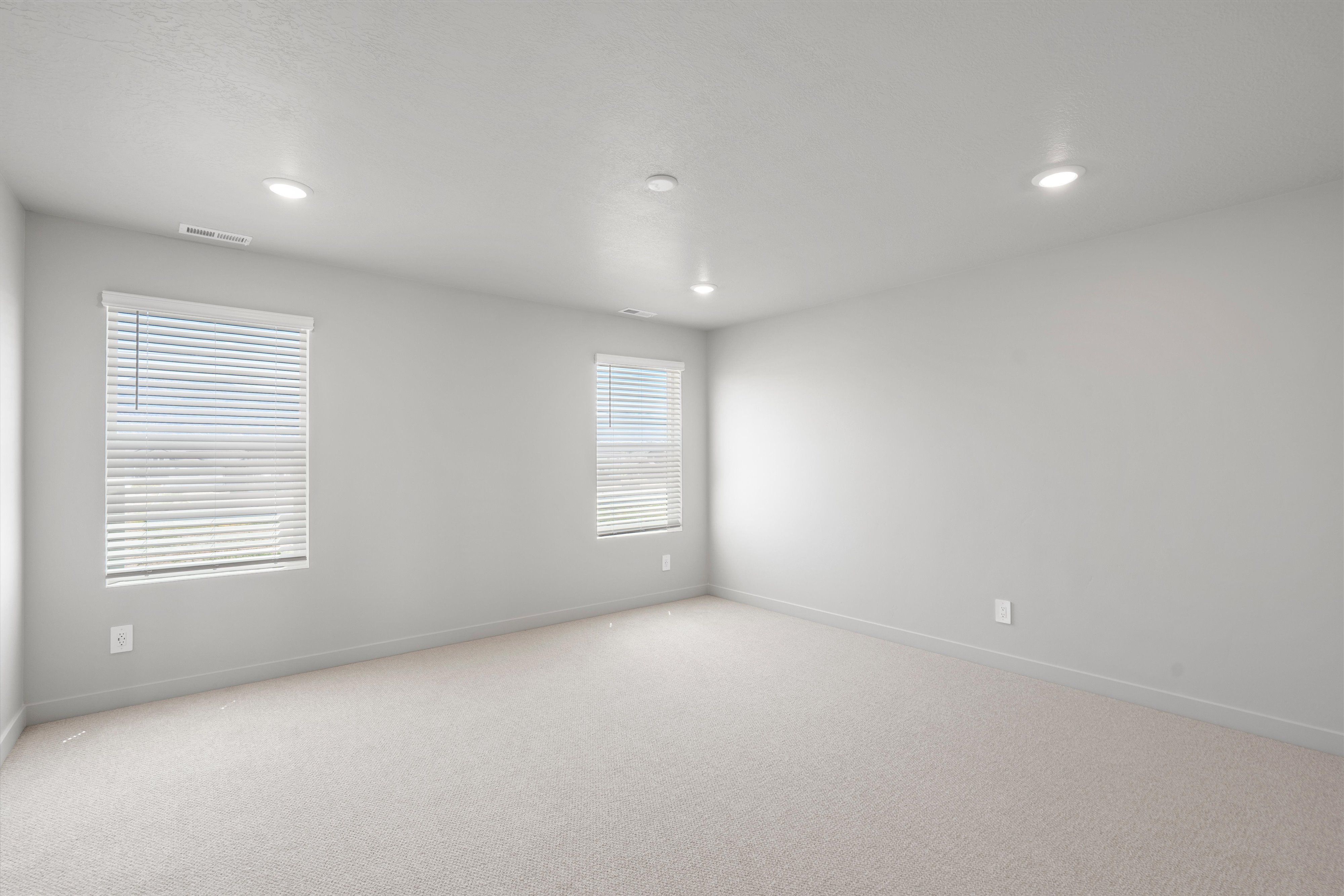 Spacious room featuring light-colored carpeting, two windows with blinds, recessed ceiling lighting, and neutral wall finishes