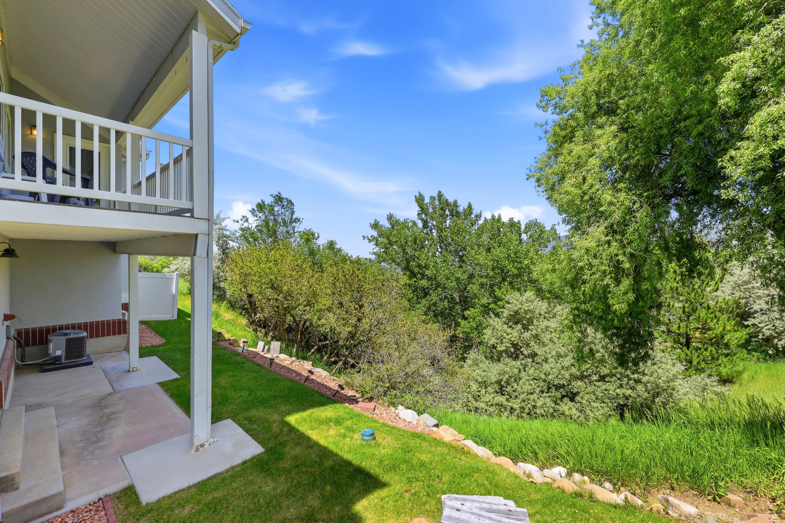 Tiered outdoor space with a concrete patio and overhead balcony featuring white railings