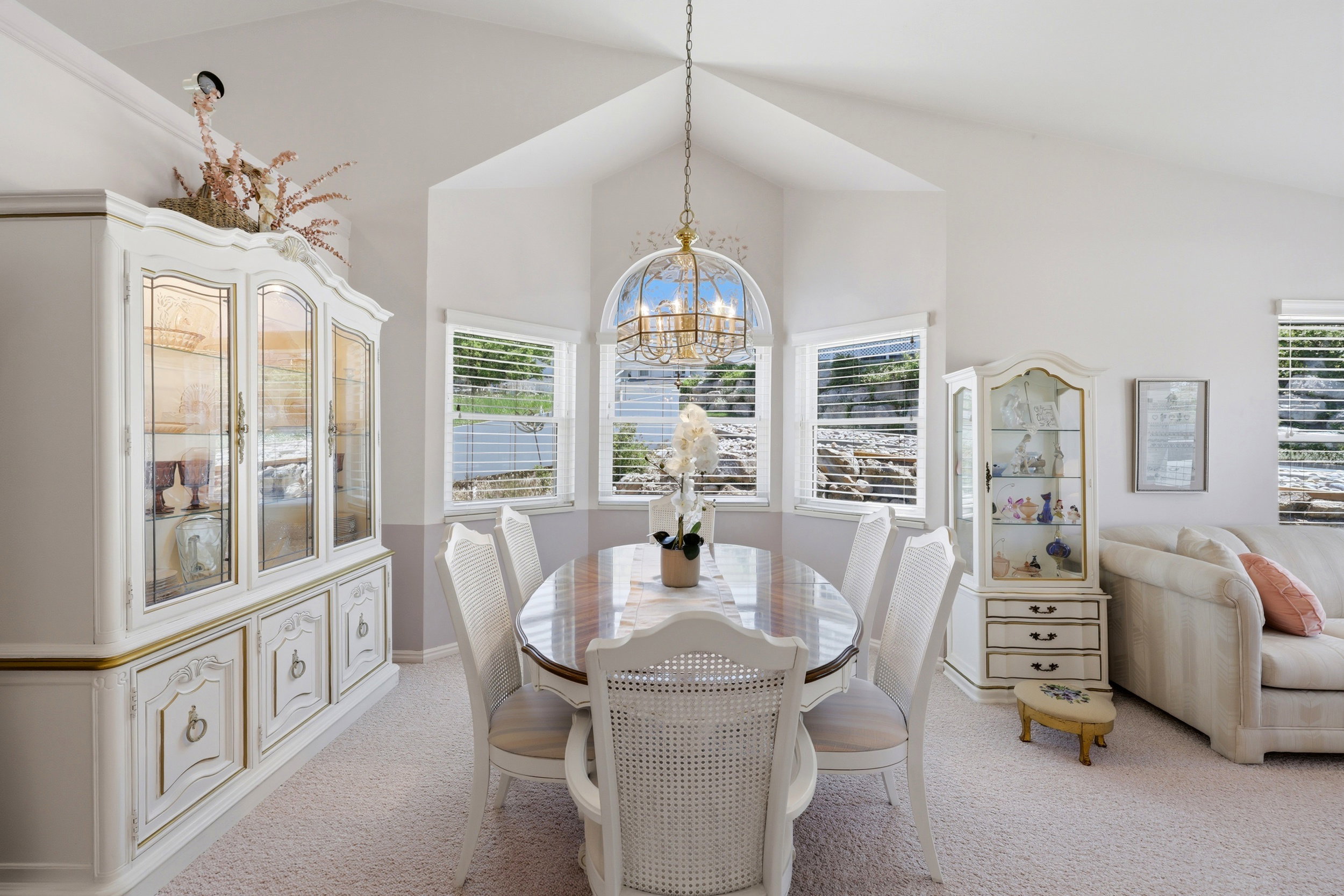 Dining area with vaulted ceilings, a central chandelier, and a bay window featuring three individual windows