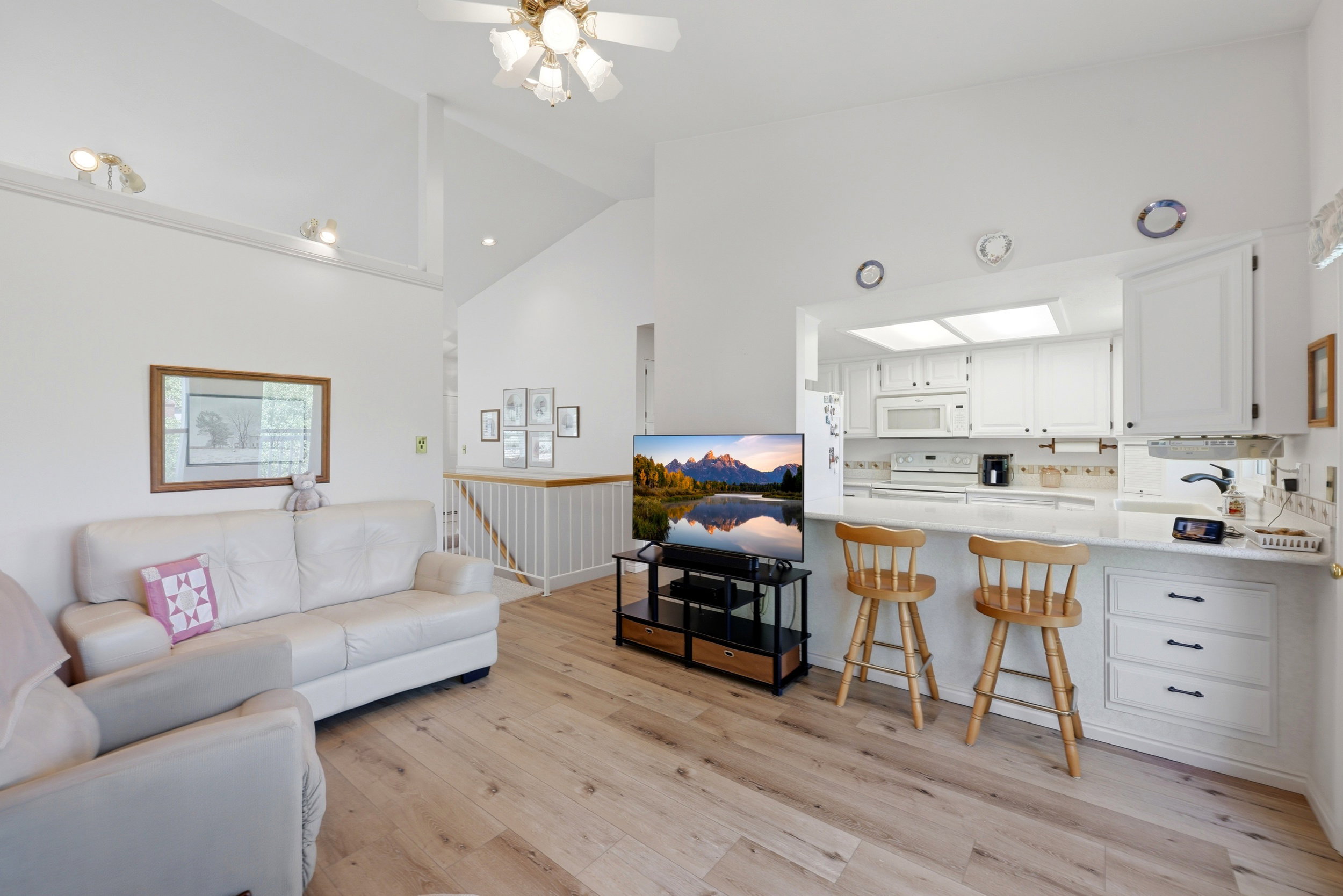 Open-concept living area featuring vaulted ceilings, wood-finish flooring, and a kitchen pass-through with a breakfast bar