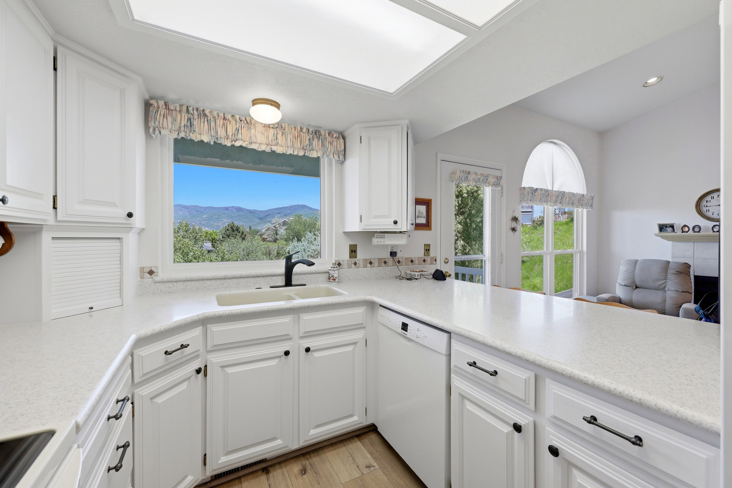 Kitchen featuring white cabinetry, light-toned countertops, a built-in dishwasher, and a window with mountain scenery