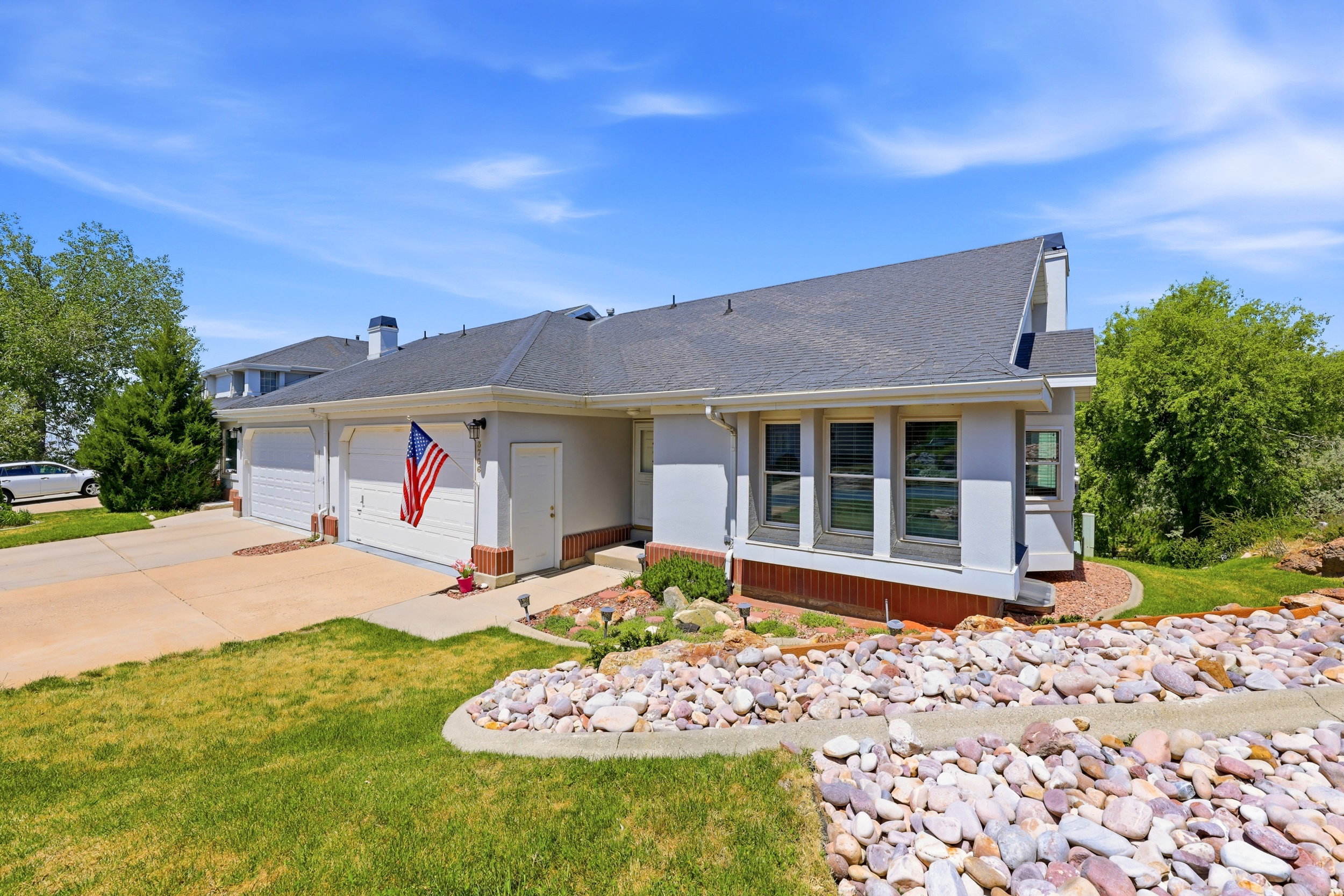 Contemporary exterior with a two-car garage, concrete driveway, multiple windows, and a rock-lined garden bed