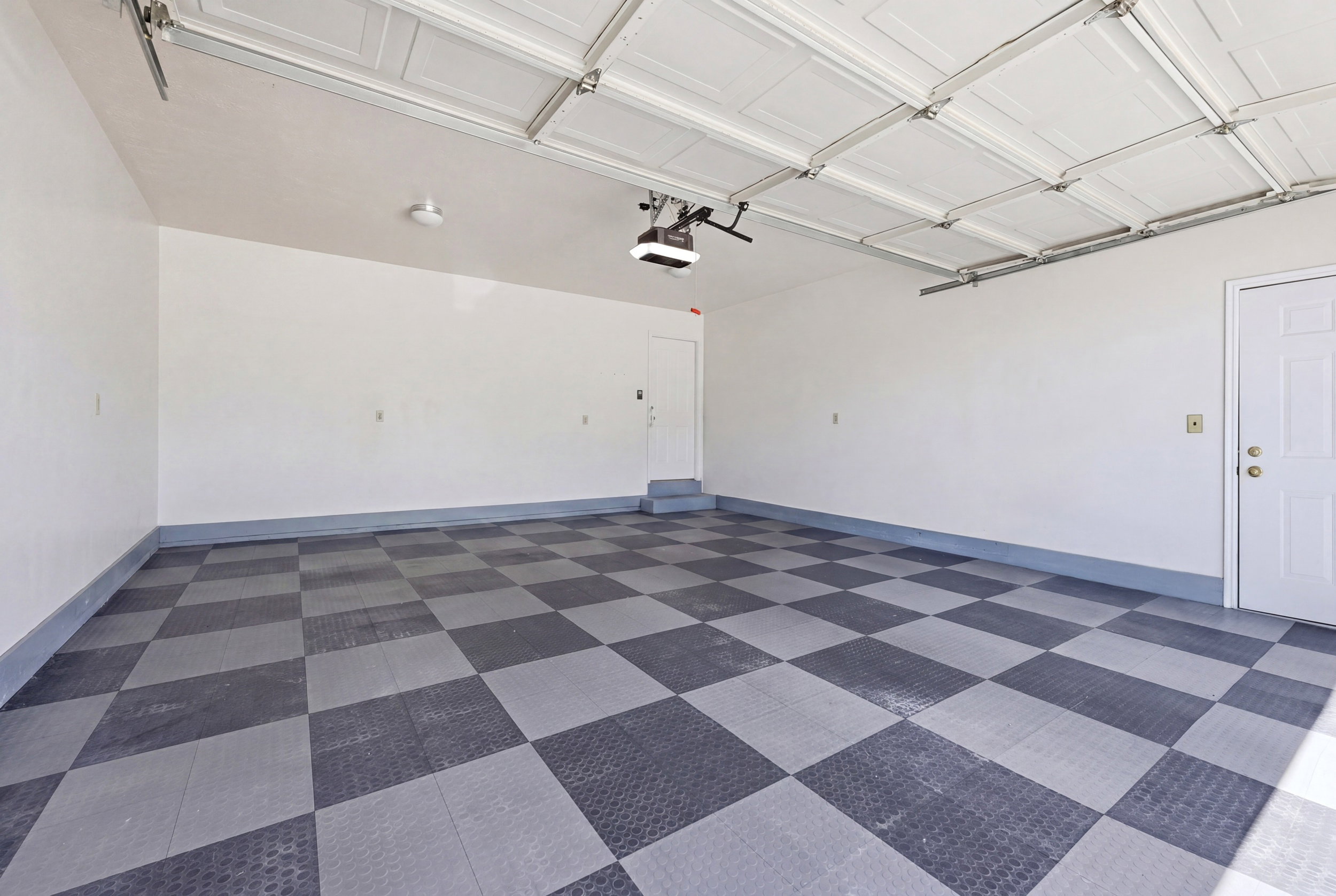 Spacious two-car garage featuring a checkerboard-patterned floor, white paneled garage door, and two white entry doors