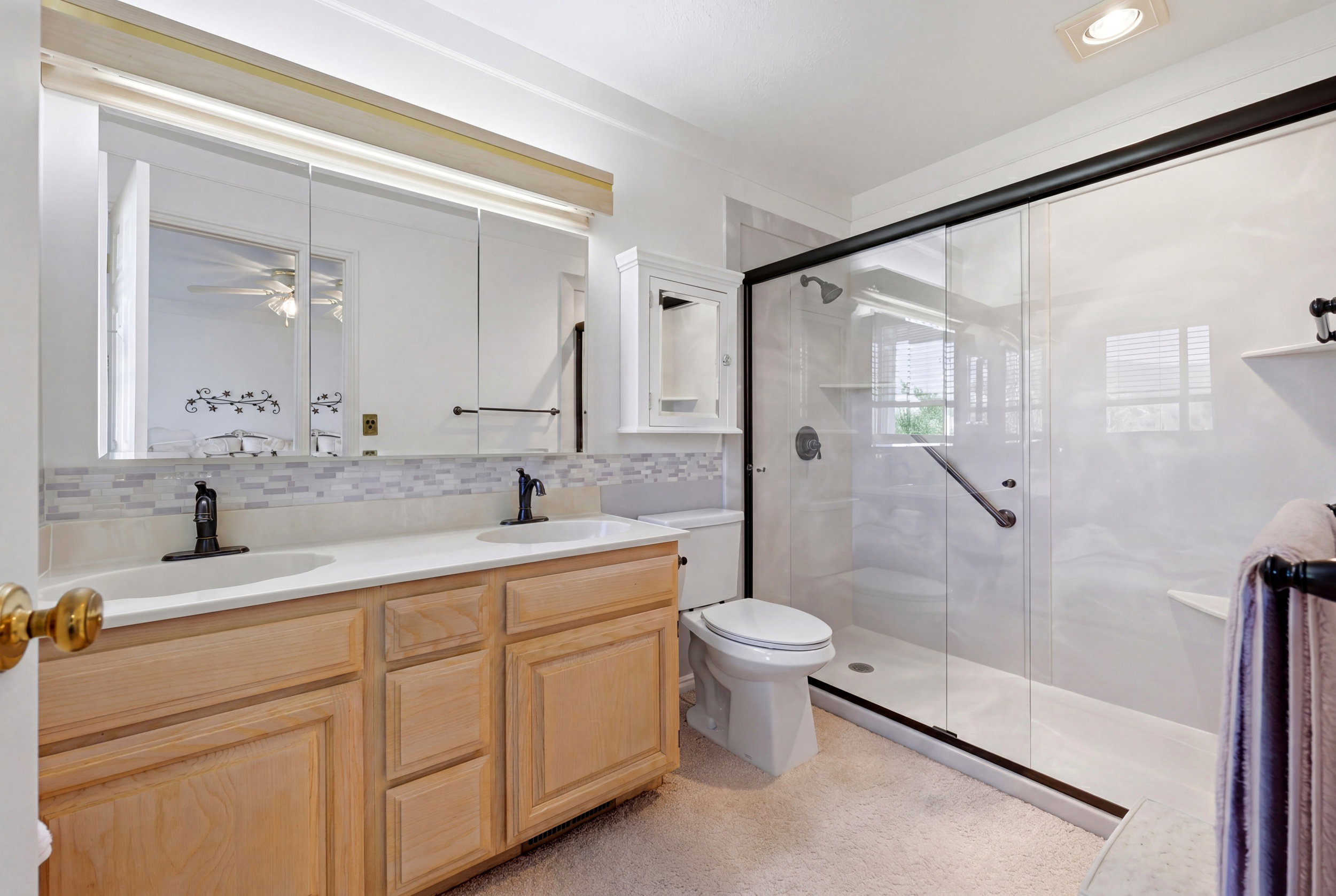 Bathroom featuring a dual vanity with light wood cabinetry, white countertops, and black fixtures
