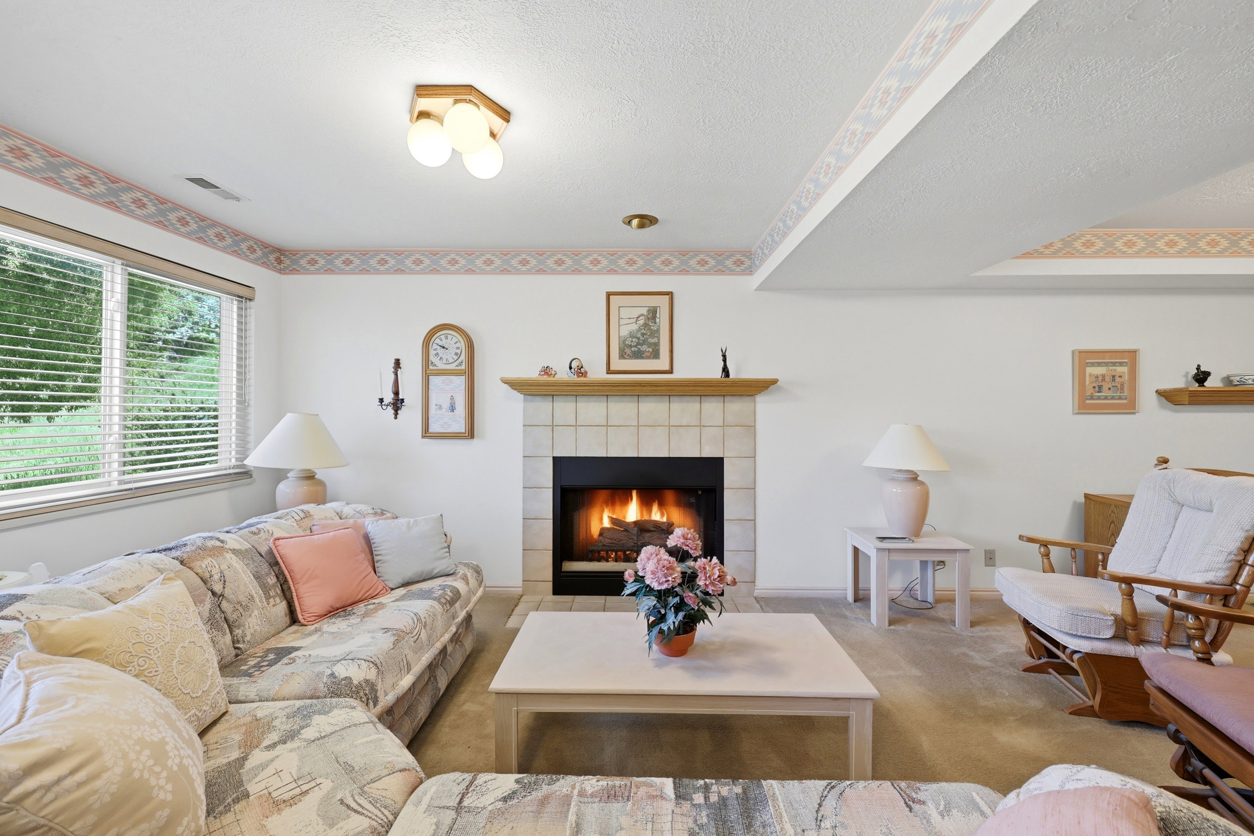 Carpeted living area featuring a tile-surround fireplace with a wood mantle, multiple windows with blinds, and white walls