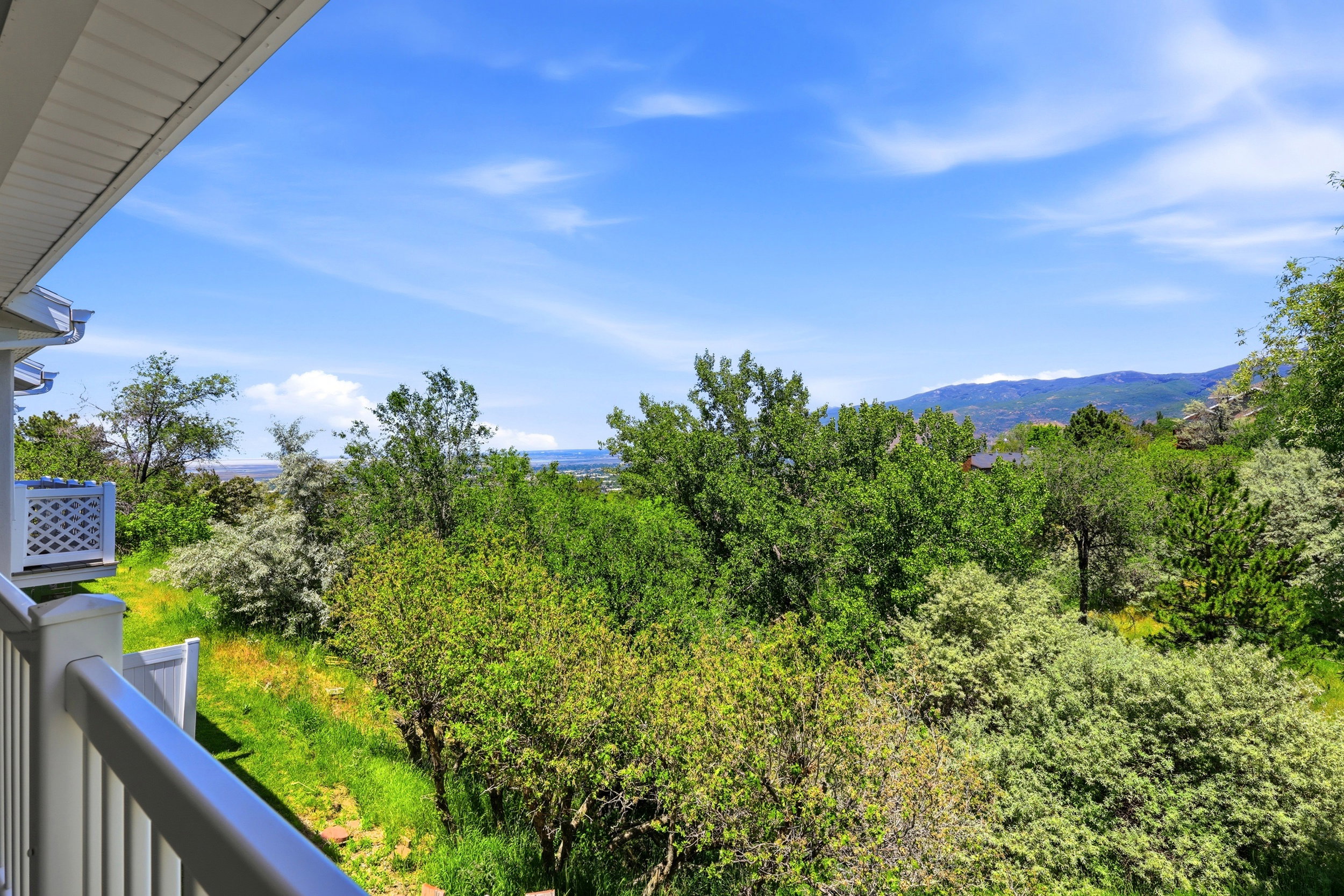 Balcony with white railing overlooking a verdant landscape, distant mountains, and a body of water