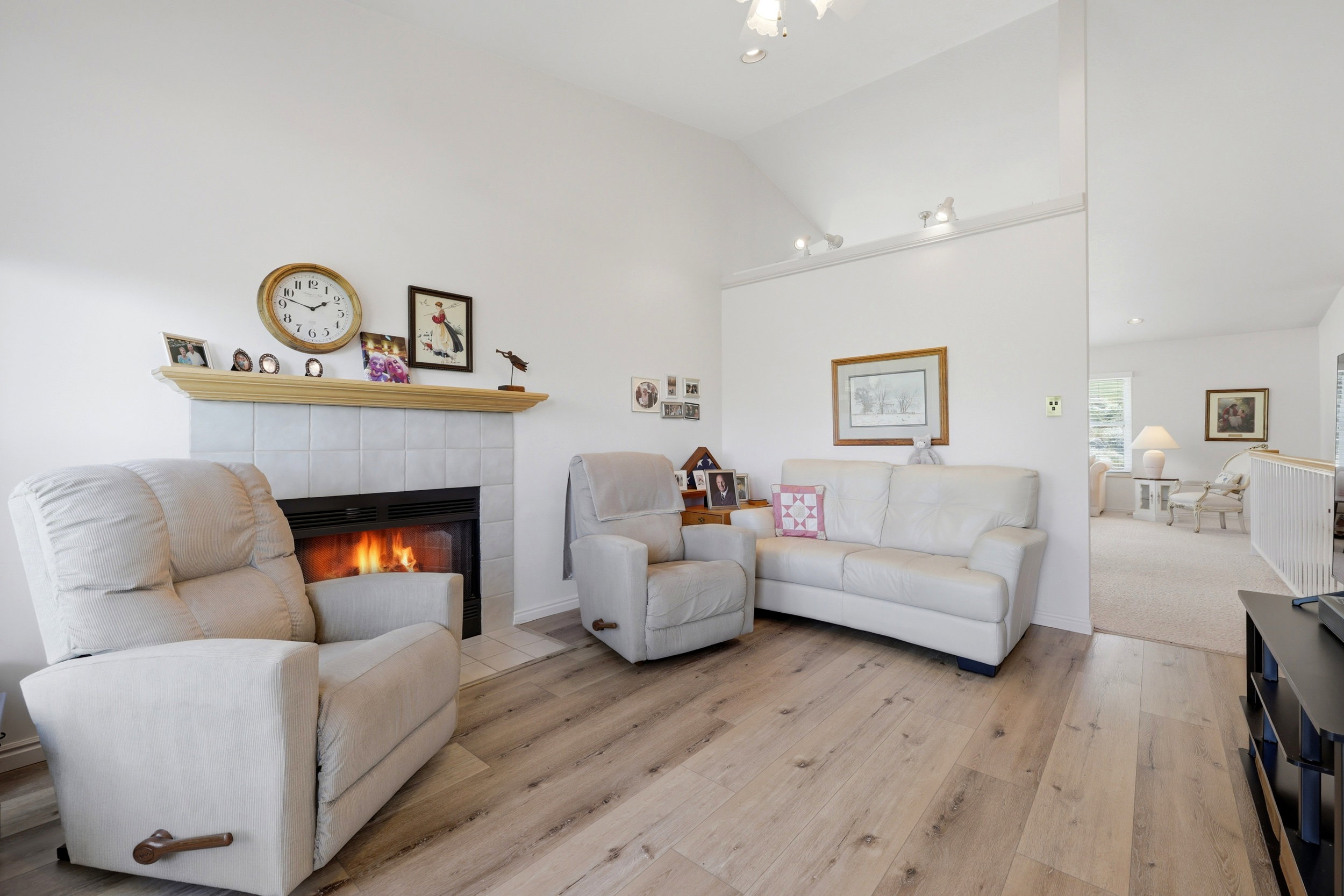 Living area featuring a fireplace with a tiled surround and wood mantel, vaulted ceilings, track lighting, and wood-finish flooring
