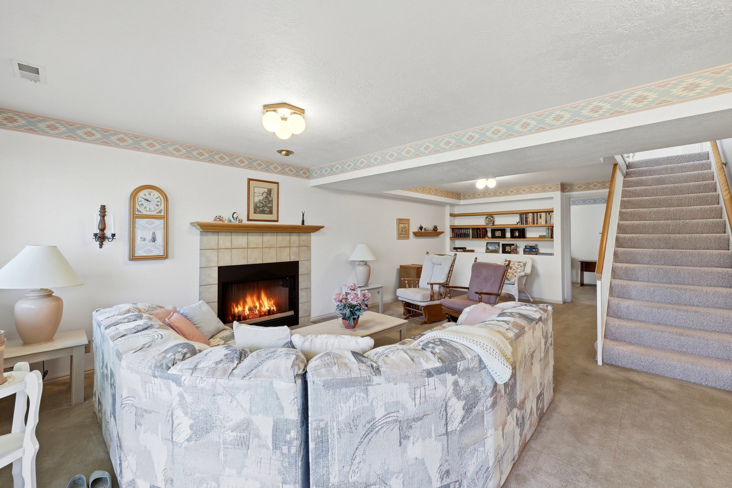 Carpeted living area featuring a tile-surround fireplace with wood mantel, built-in shelving, and a carpeted staircase with wood handrail