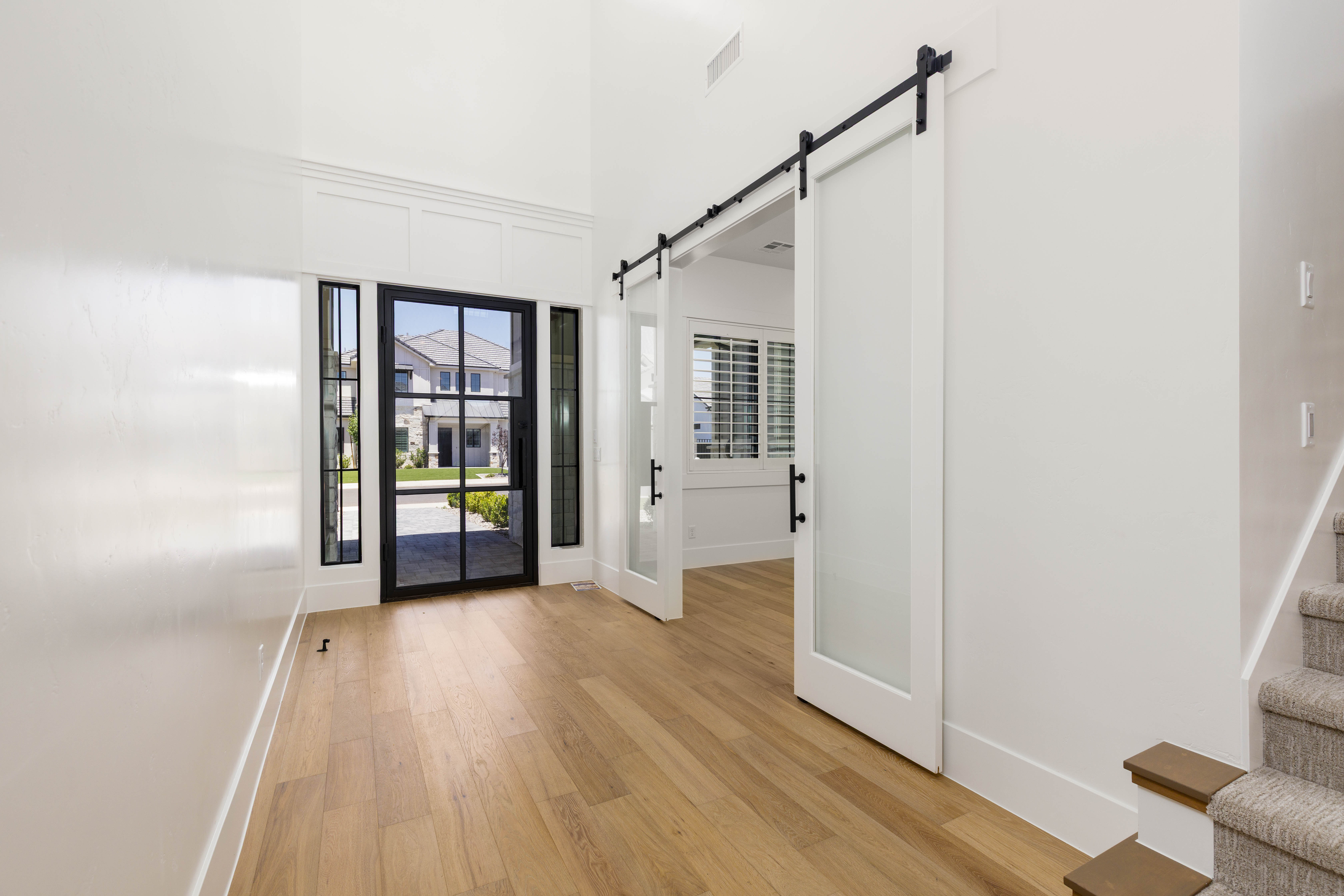 Entryway featuring a black-framed glass door with sidelights, wood-finish flooring, a white trim accent wall, and frosted glass barn doors