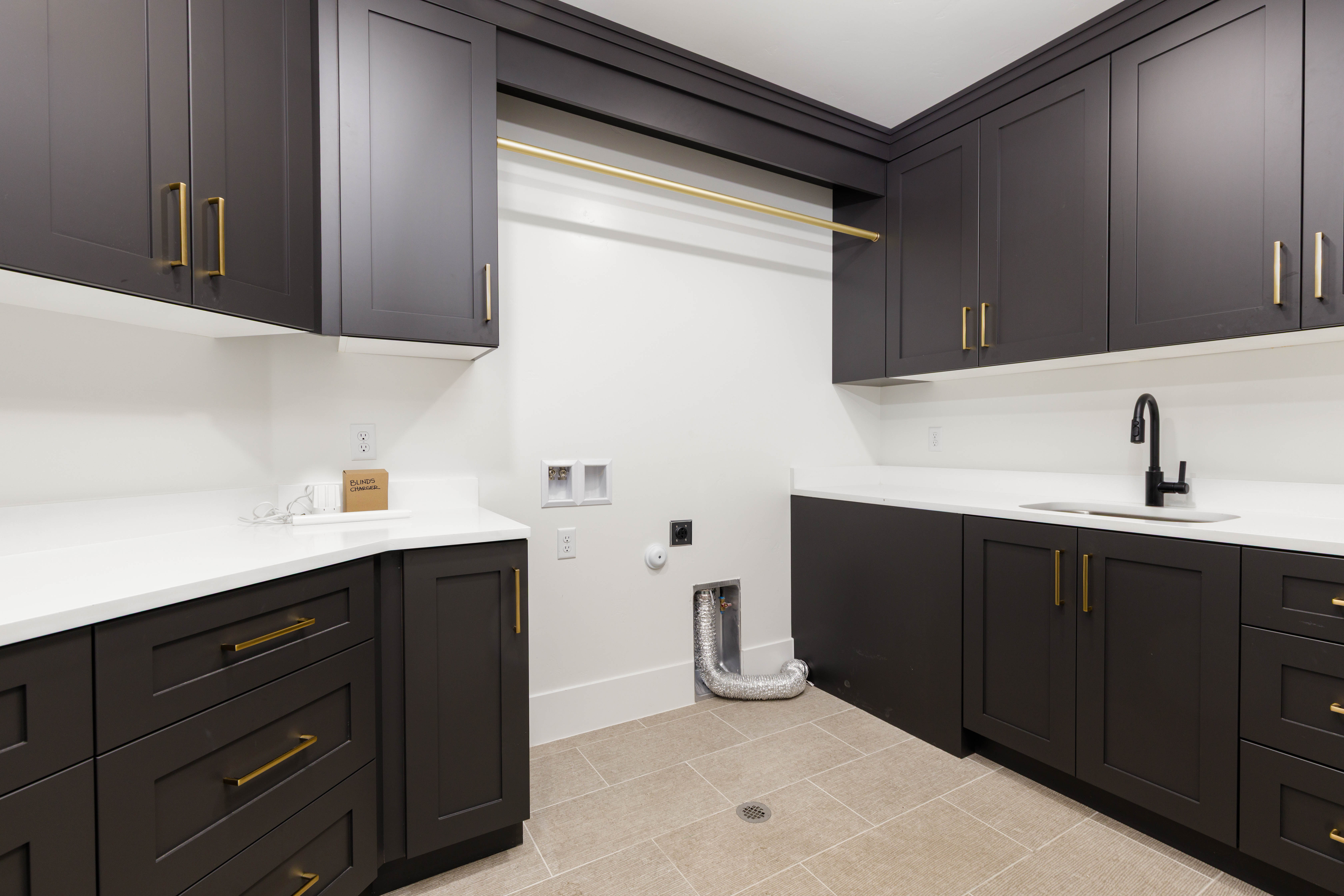 Laundry space featuring dark shaker-style cabinetry with brass hardware, white countertops, and a utility sink with a matte black faucet