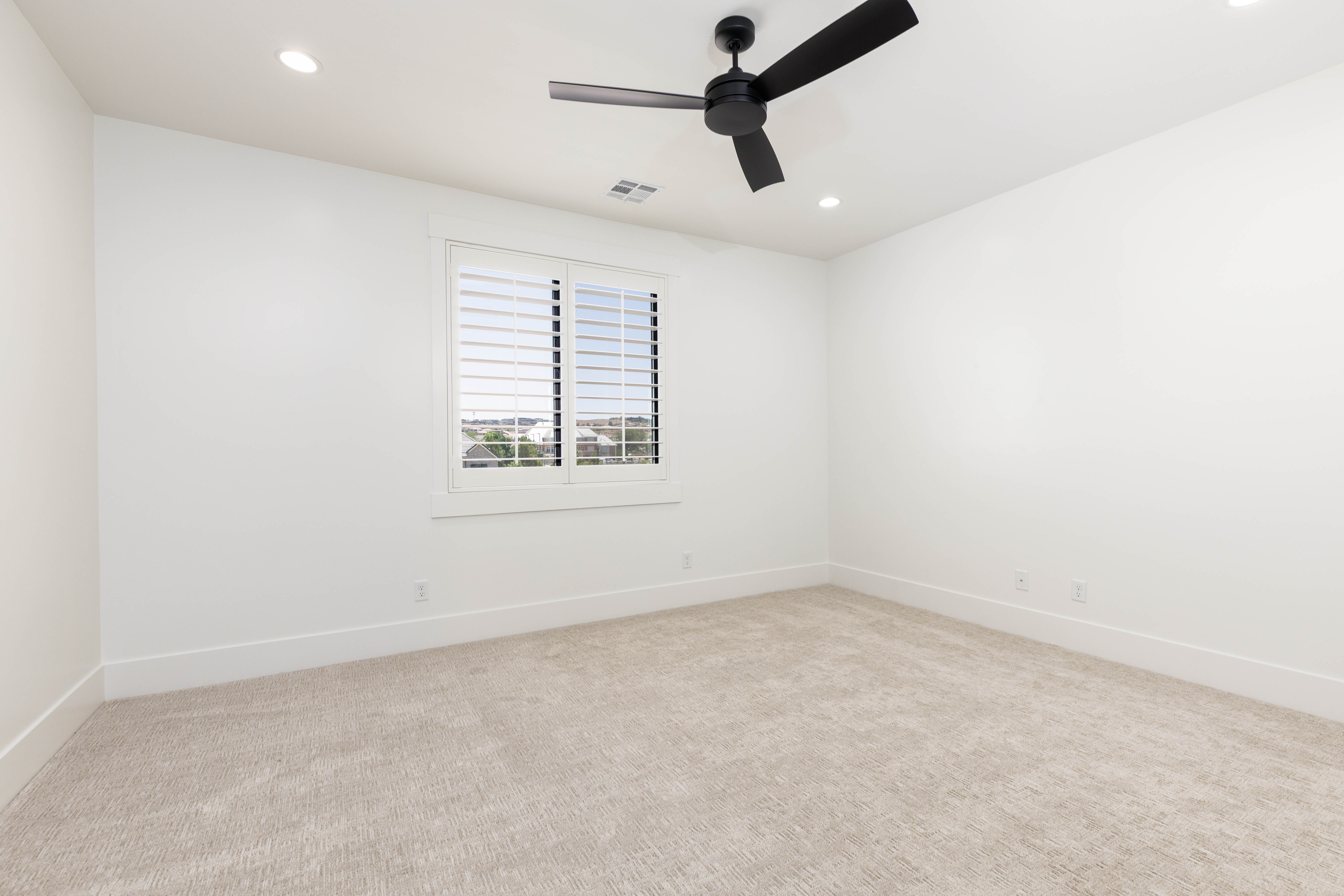 Bright interior space featuring a window with white louvered shutters, recessed lighting, a ceiling fan with black blades, and light-toned carpet flooring