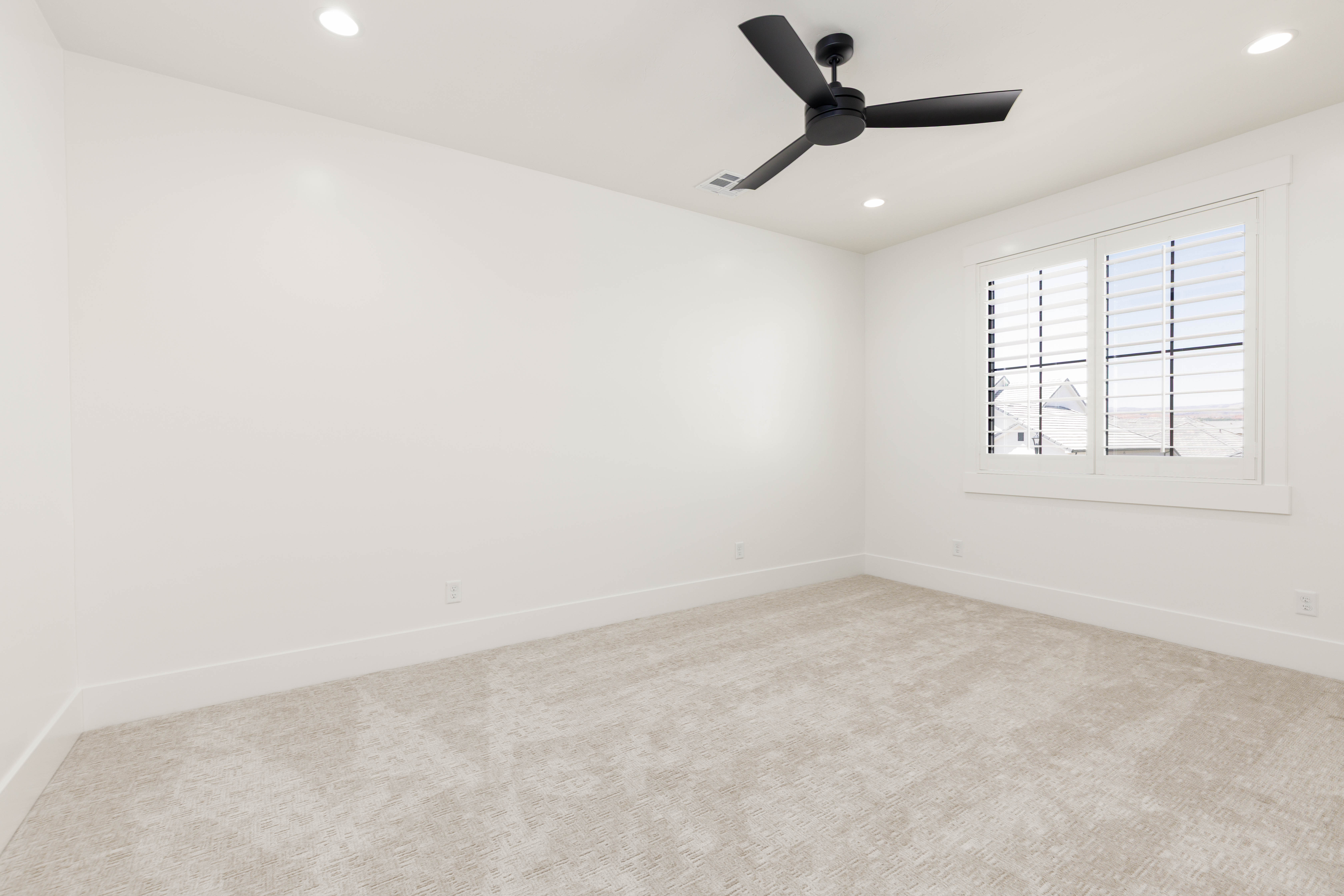 Spacious room featuring neutral carpeting, white walls, and a window with white plantation shutters