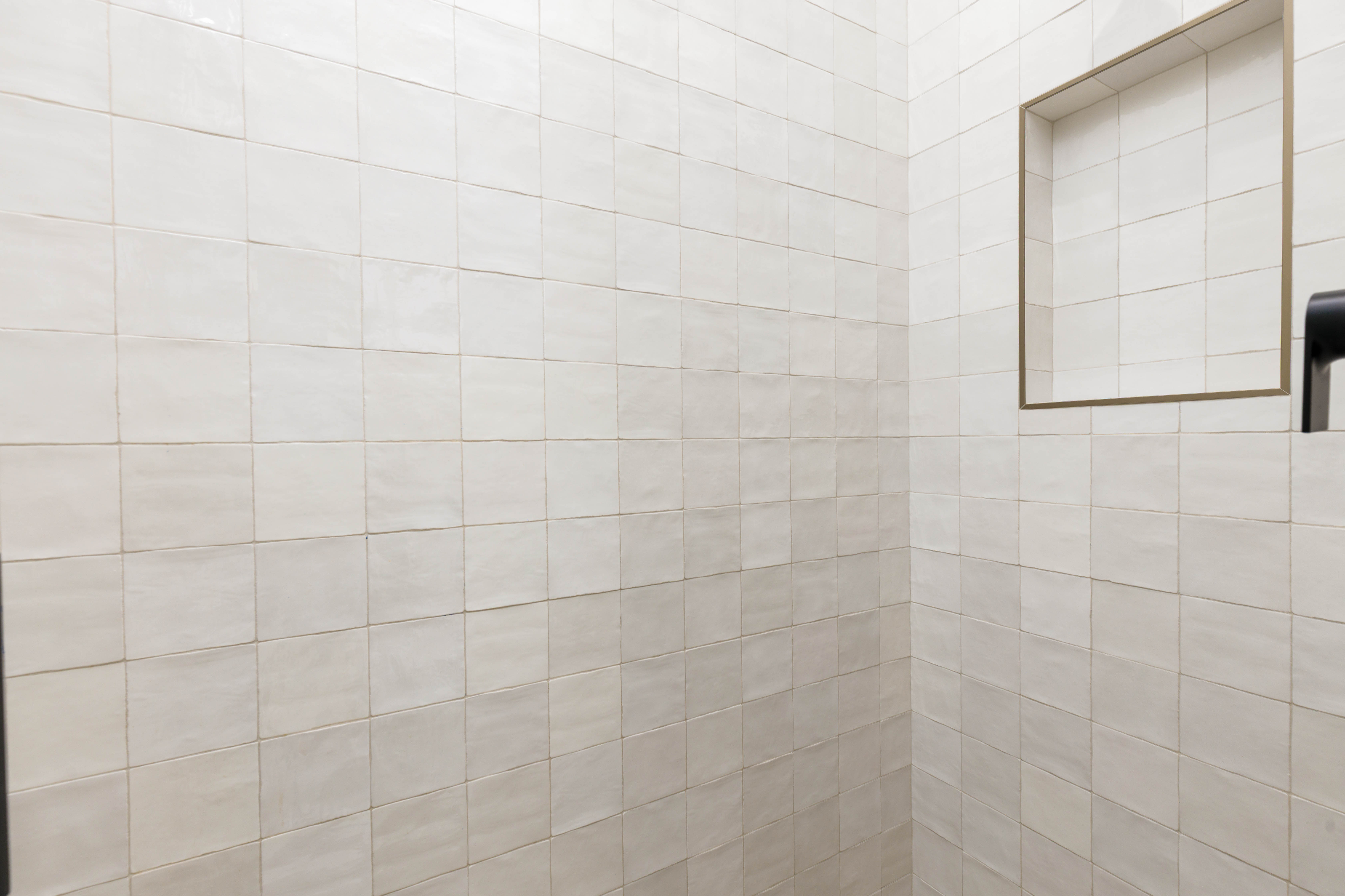Tiled shower enclosure featuring light-toned square tiles and a recessed niche with a contrasting trim
