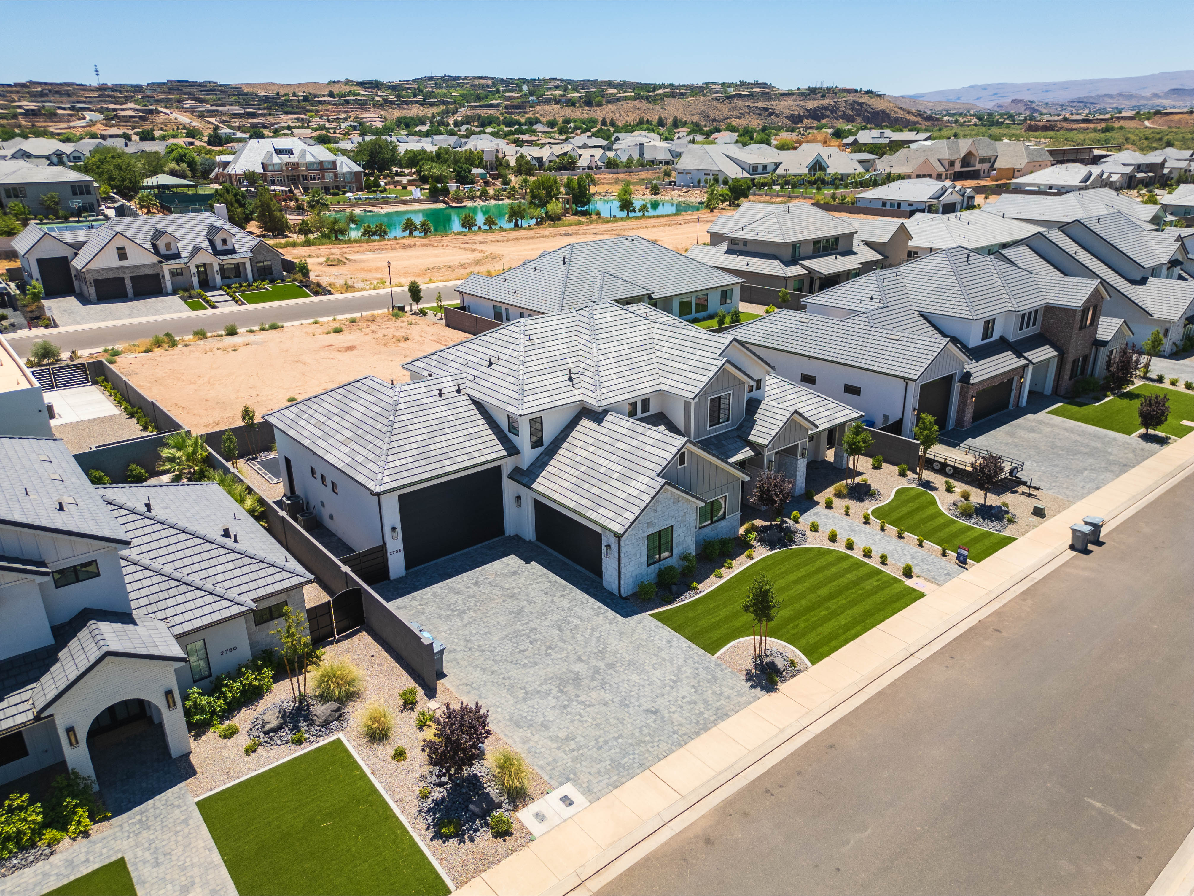 Modern-style residence featuring a patterned paver driveway, dark-tiled roof, and manicured landscaping with artificial turf accents