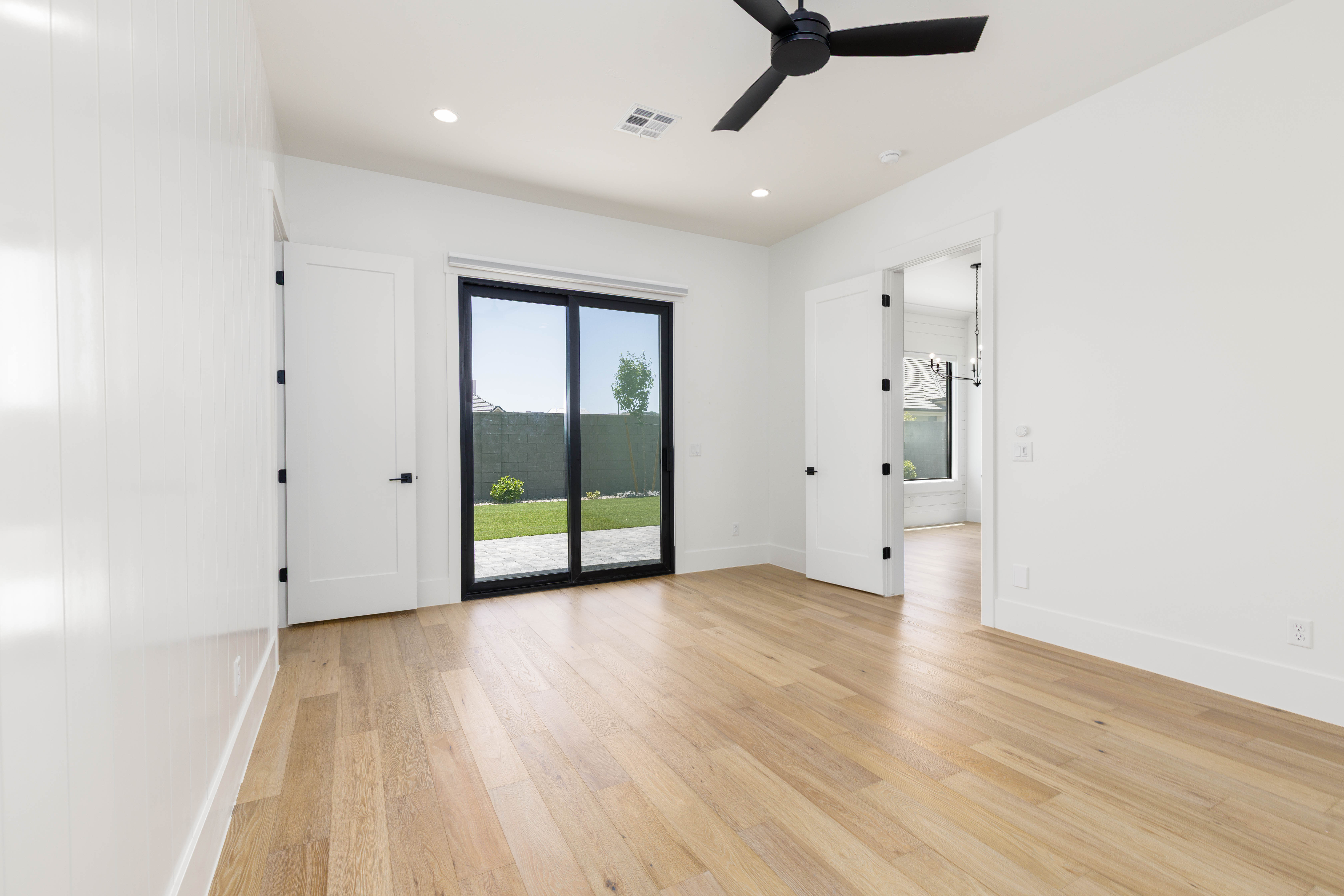 Spacious room featuring light wood-finish flooring, white walls, and a black ceiling fan