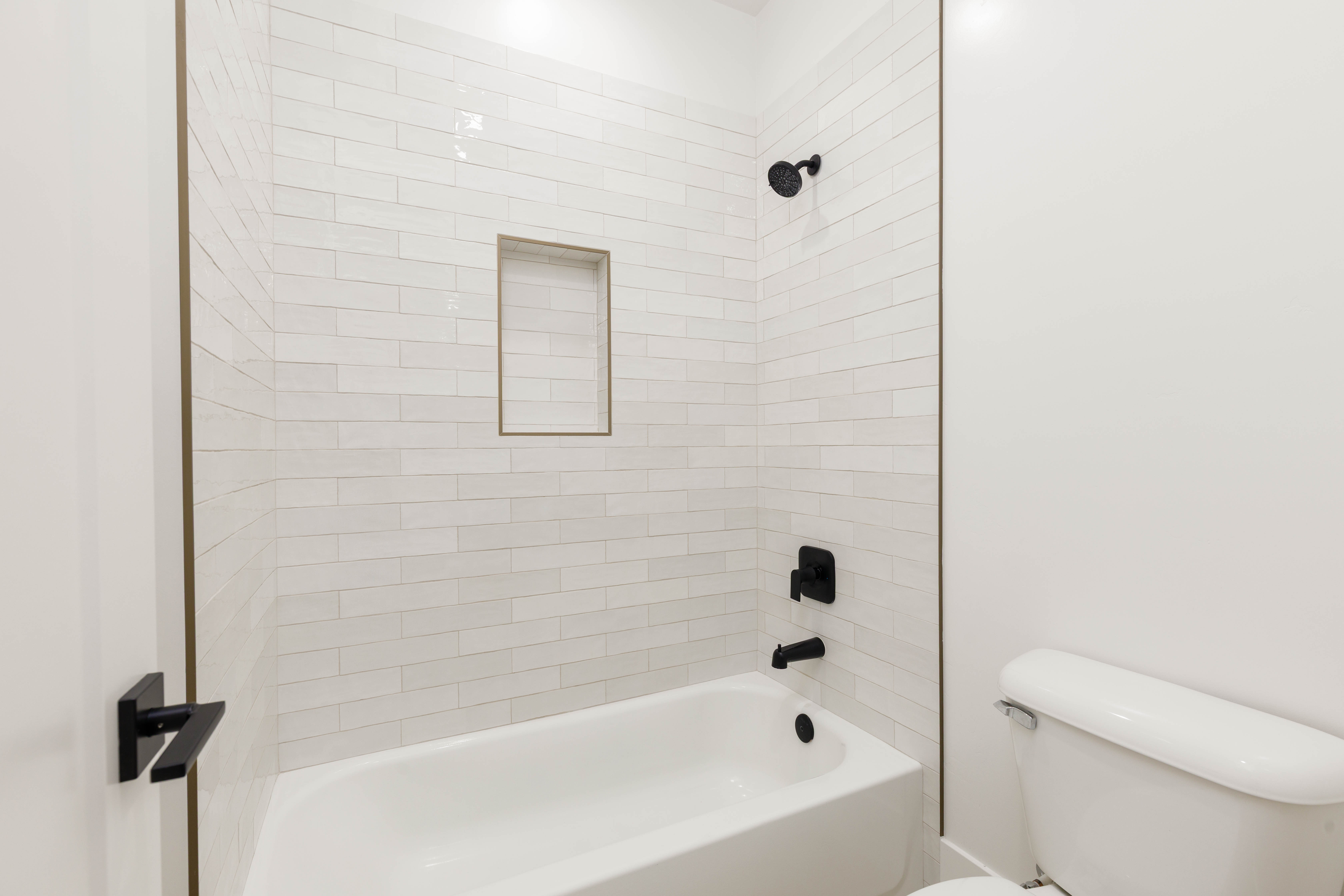 Bathtub shower with white subway tile surround, recessed niche, and matte black fixtures