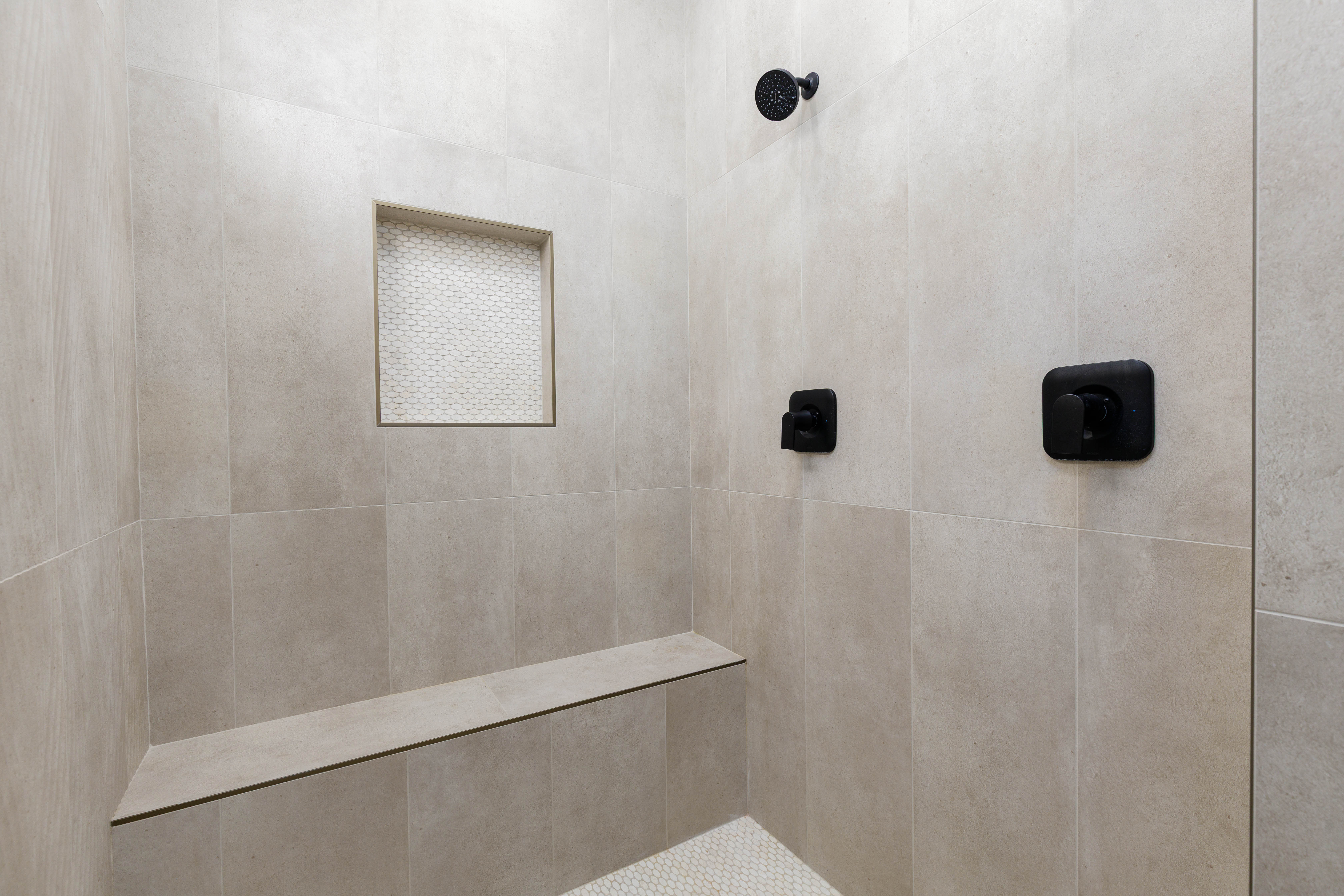 Shower stall featuring large format neutral-toned wall tiles, matte black fixtures, and a built-in bench