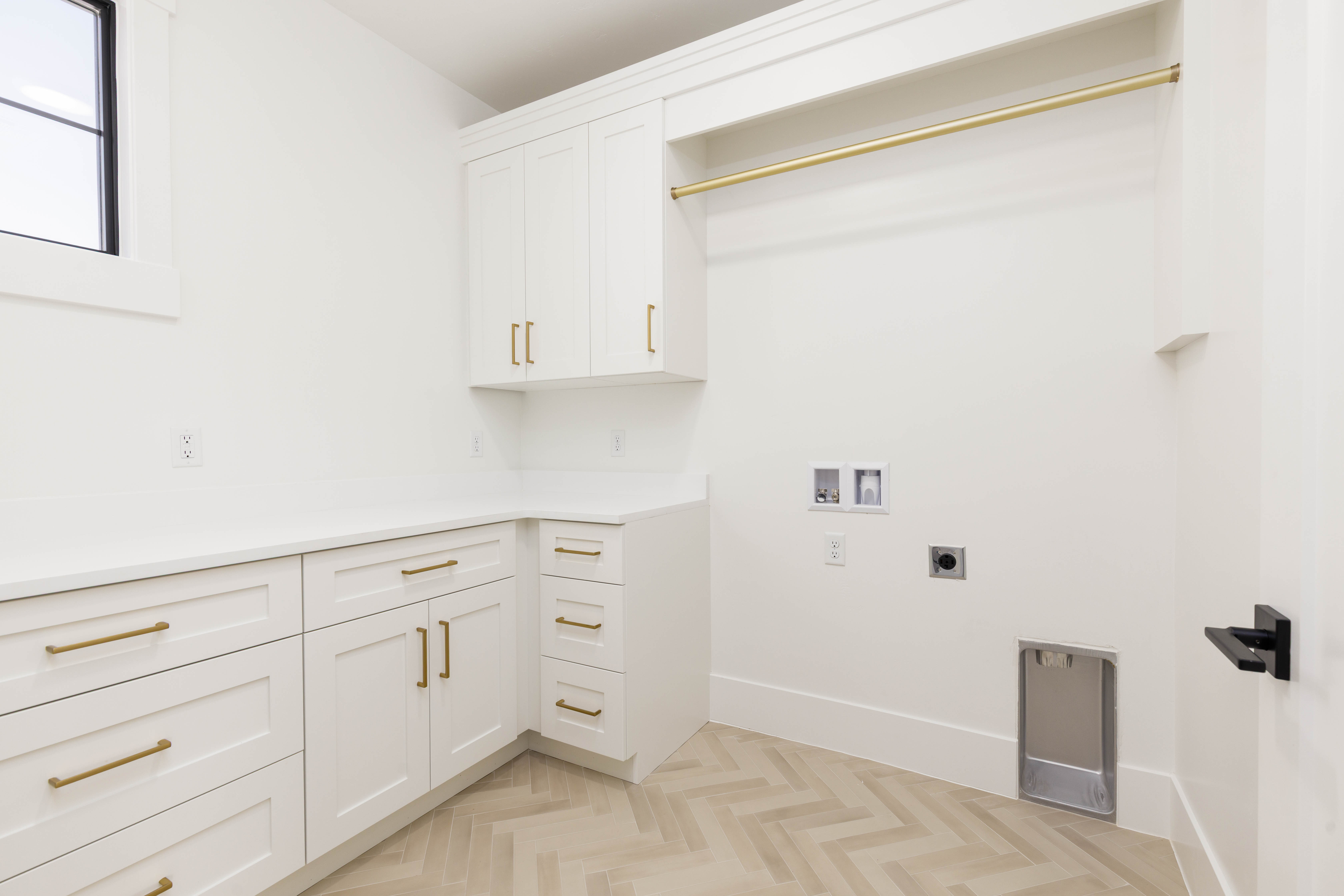 Utility room featuring white cabinetry with gold-finish hardware, light wood-finish herringbone flooring, a built-in hanging rod, and a window for natural light
