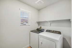 Dedicated laundry area featuring a window with white blinds, overhead shelving, and light wood-finish flooring
