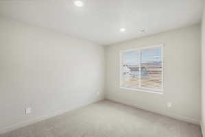 Bright room featuring light grey walls, recessed ceiling lighting, a window with blinds, and soft grey carpeting