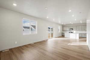 Spacious open-concept living area featuring wood-finish flooring, recessed lighting, and large windows with blinds