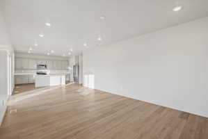 Open-concept living space featuring wood-finish flooring, recessed lighting, and a white kitchen with a center island