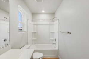 Bathroom featuring a white tub-shower combination unit, white toilet, and a window with white blinds