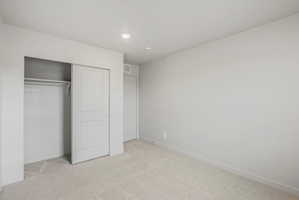 Neutral-toned room featuring light carpet flooring, white baseboards, and a built-in closet with sliding panel doors and a clothing rod