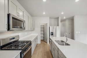 Open-concept kitchen featuring light-toned cabinetry, stainless steel appliances, light countertops, wood-finish flooring, and recessed lighting