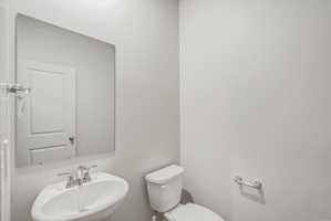 Powder room featuring a pedestal sink with a chrome faucet, a rectangular wall-mounted mirror, and a modern toilet