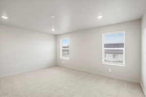Spacious interior with neutral-toned walls, plush carpeting, recessed lighting, and two windows with blinds