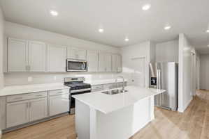 Kitchen featuring light-toned cabinetry, stainless steel appliances, a center island with an undermount sink, and recessed lighting