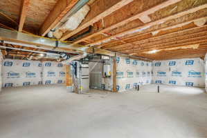 Unfinished basement space featuring a concrete floor, exposed wood ceiling joists, and insulated perimeter walls