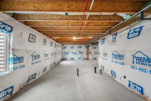 Unfinished basement space featuring exposed wood joists and subflooring, a concrete floor, and wrapped exterior walls