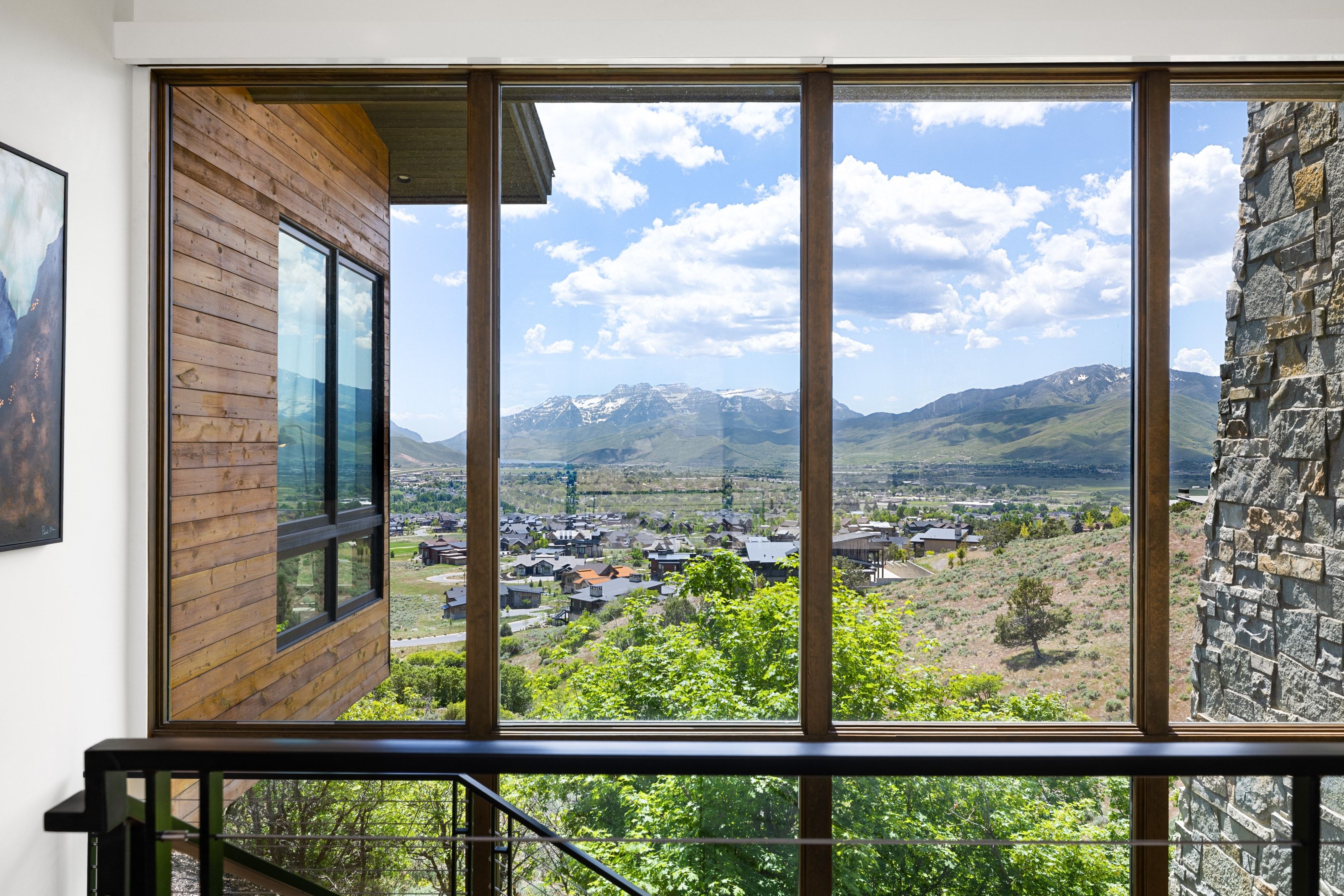 Floor-to-ceiling window system with dark wood-finish framing, integrated into natural stone and horizontal wood siding